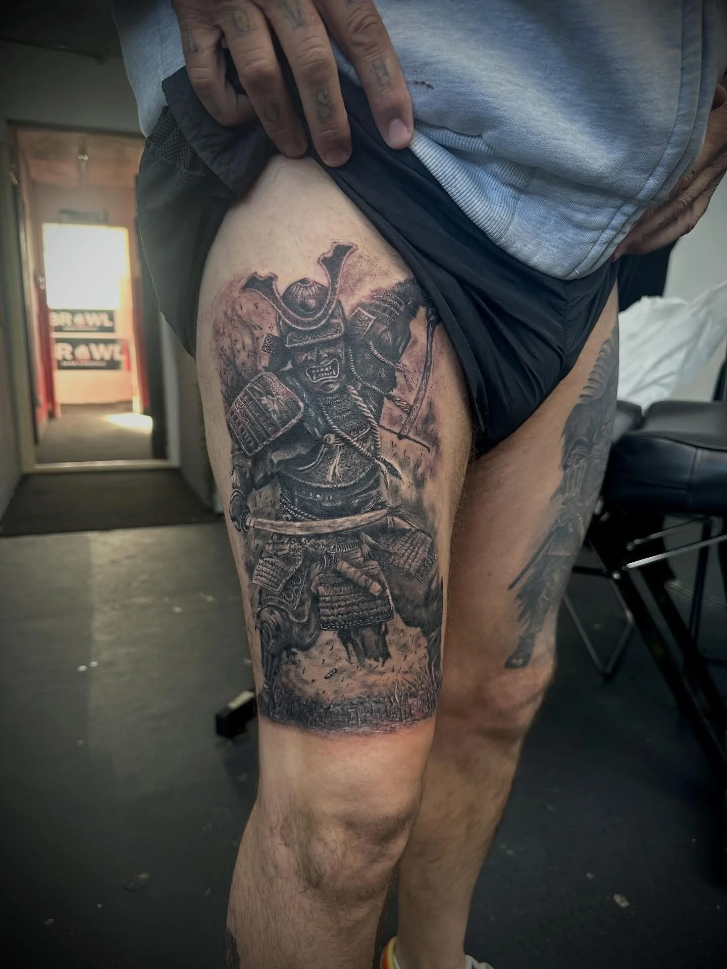 Tattoo of a samurai warrior in armor, holding a katana, on a man's thigh.