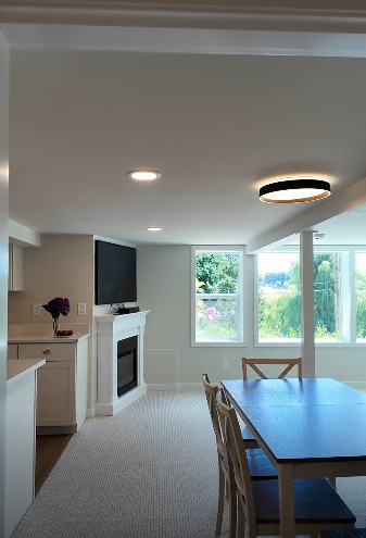 A fully remodeled downstairs bonus suite showcasing an open concept living space with an electric fireplace, mounted tv, large living room windows bring in plenty of daylight to this basement.