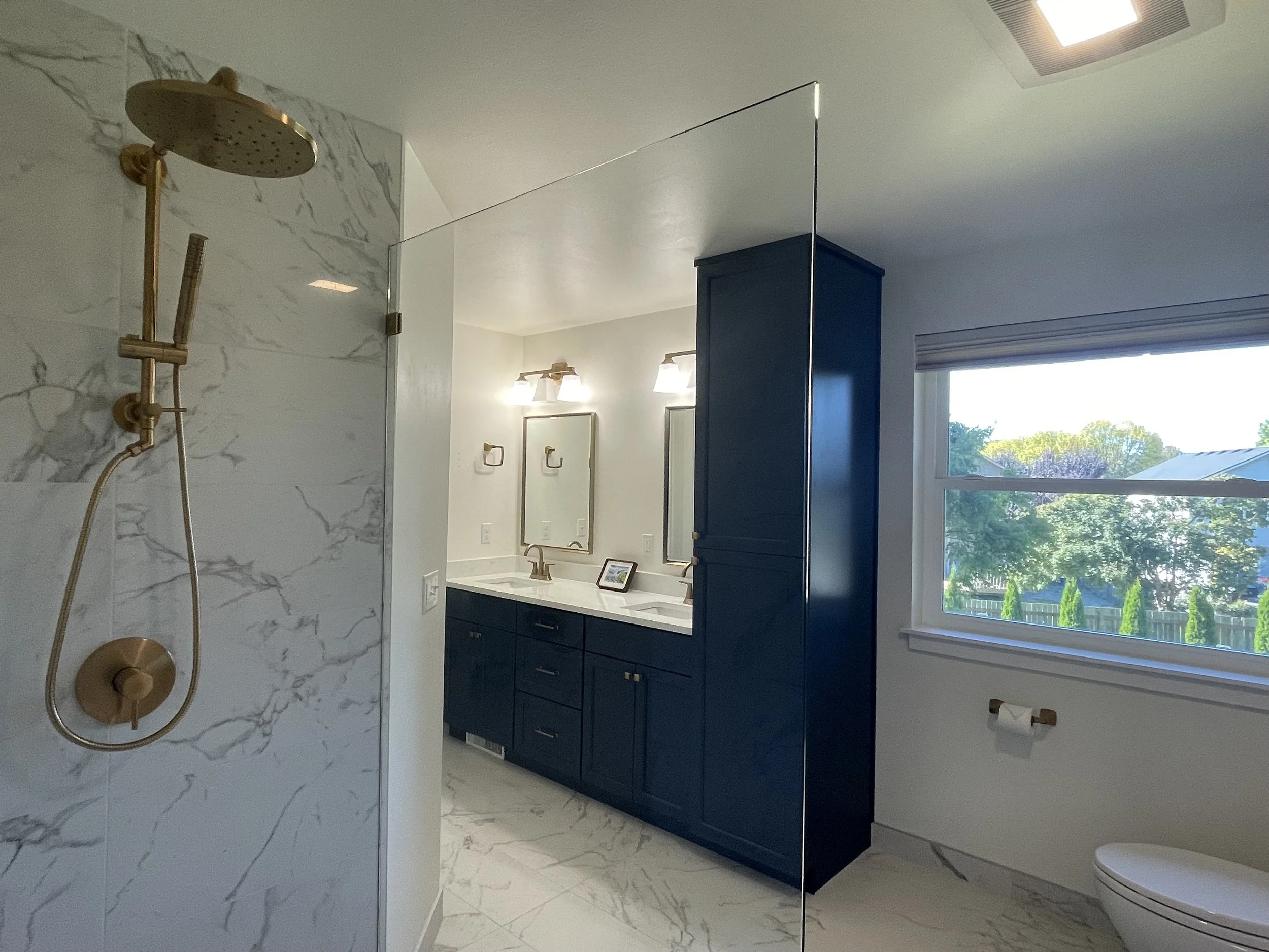 Monroe, WA primary en-suite bathroom remodel featuring a custom walk-in shower with marble-look tile, frameless glass, floating toilet and a navy blue double vanity.
