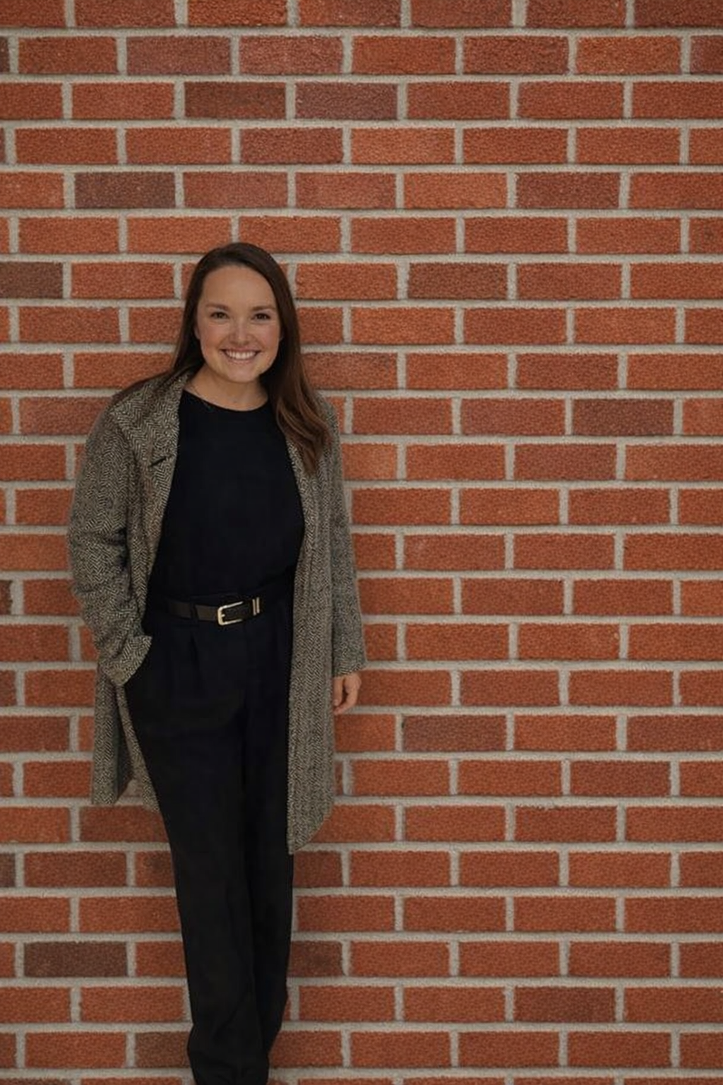 A smiling woman, wearing black, standing in front of a brick wall.