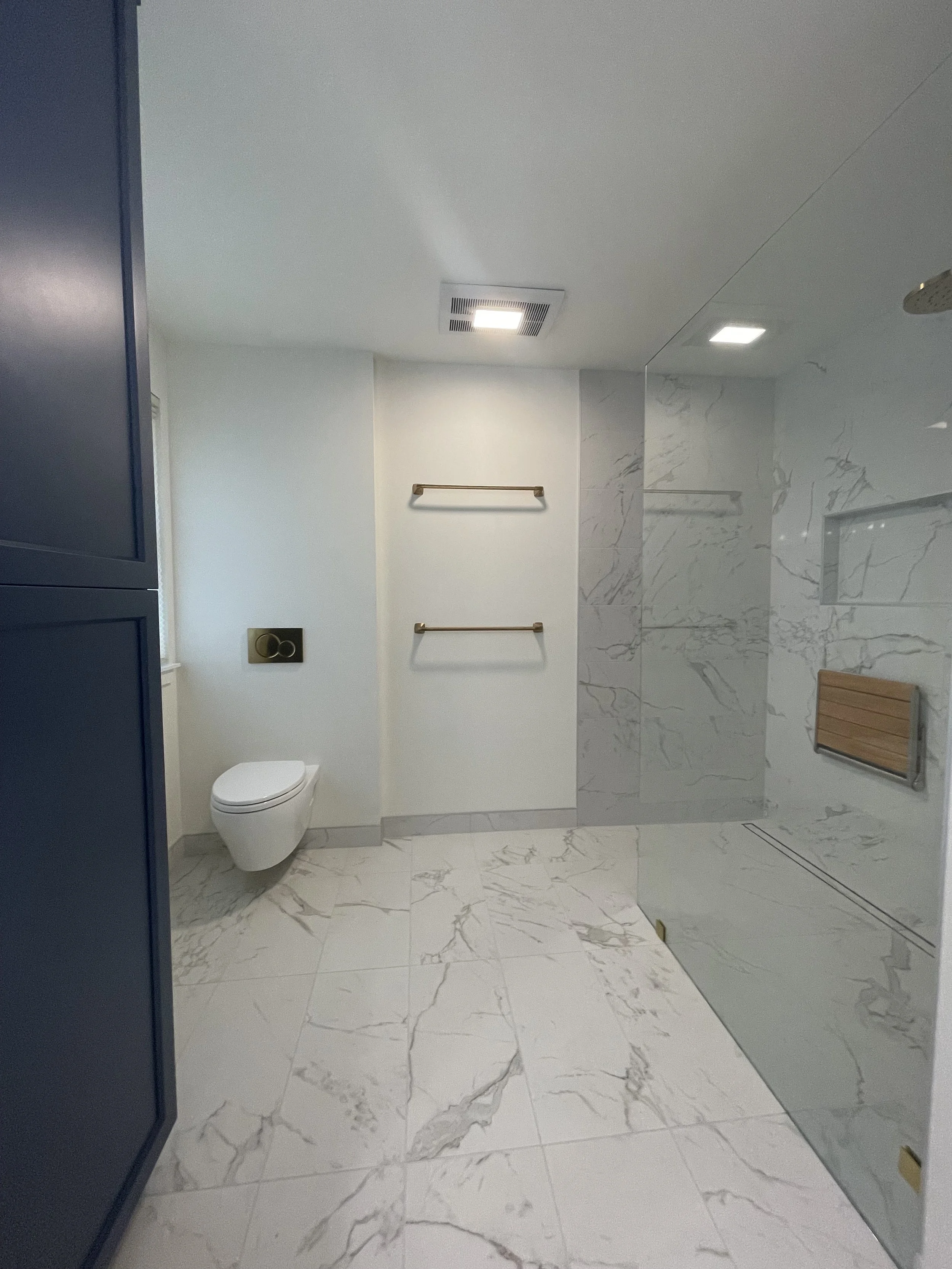 Primary bathroom remodel in Monroe, WA featuring a spacious walk-in shower, floating toilet, frameless glass enclosure, marble-look tile and brushed gold fixtures.
