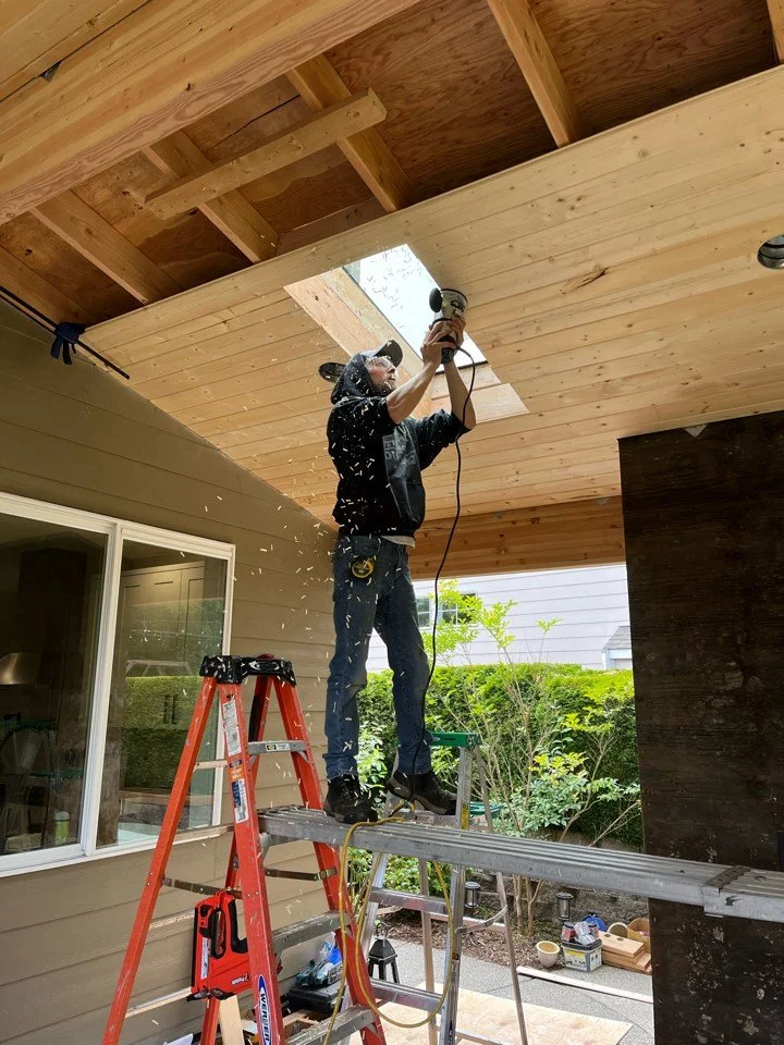 Nordic Home Solutions team in action working on building covered outdoor patio with built-in skylights. Featuring an outdoor living space with a custom built outdoor gas fireplace in Mill Creek, WA.