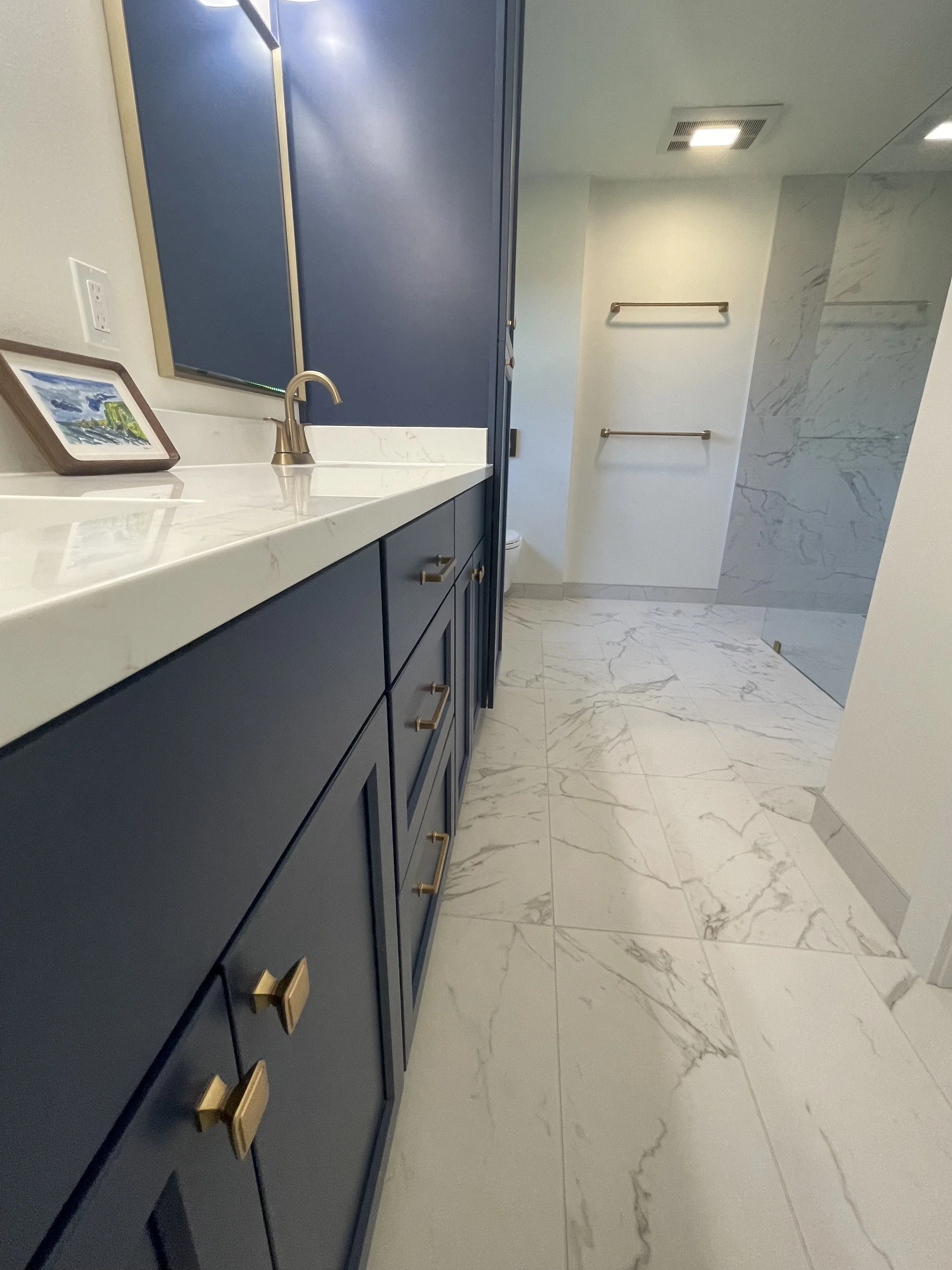 Custom navy blue double vanity in a Monroe, WA primary bathroom remodel with white countertops, undermount sinks, brushed gold faucets and coordinating mirrors.
