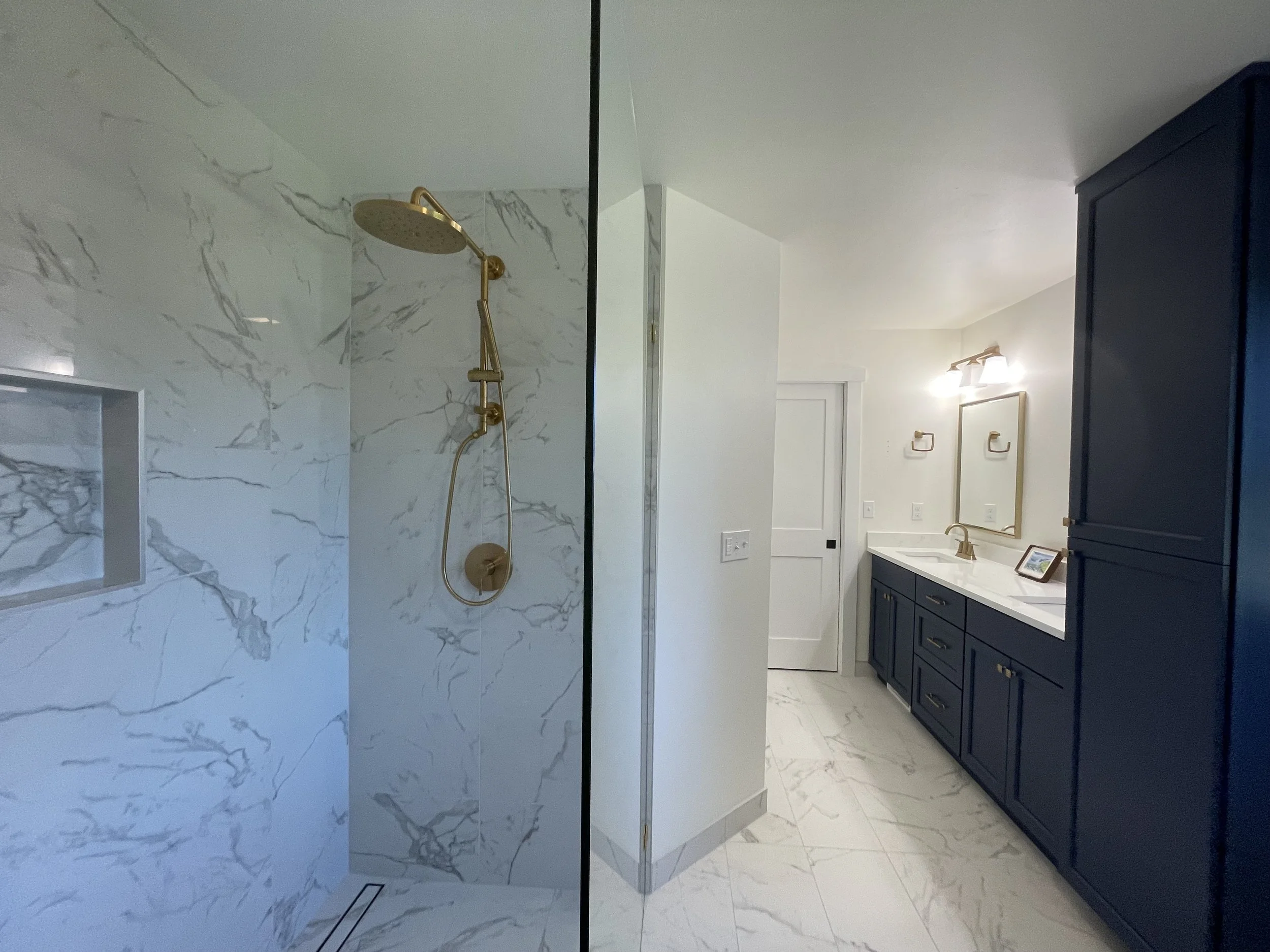 Primary bathroom remodel in Monroe, WA featuring a spacious walk-in shower, frameless glass enclosure, marble-look tile and brushed gold fixtures.