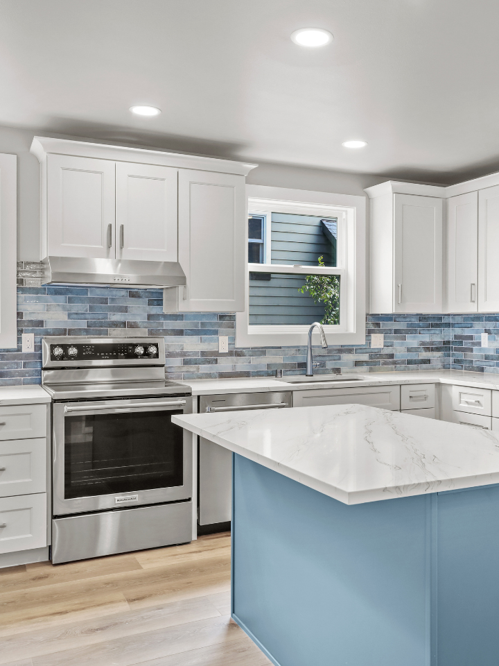 Modern kitchen remodel showcasing white kitchen cabinets, with marble countertops, blue tile backsplash, stainless steel appliances, and a window.