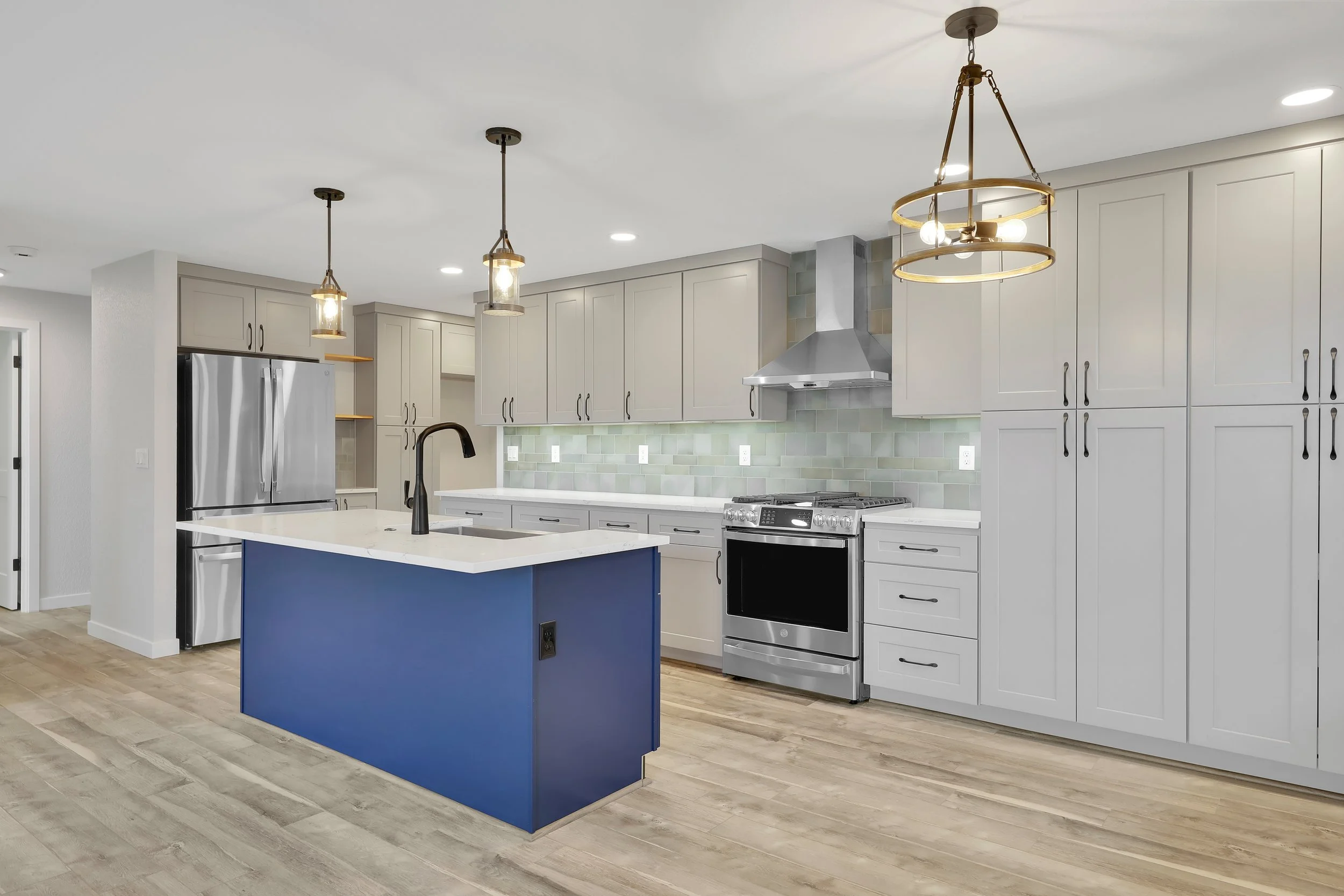 Modern kitchen remodel by Nordic Home Solutions in Snohomish County. Featuring a custom built blue island, griege colored cabinets, stainless steel appliances, custom tile backsplash and pendant lighting.
