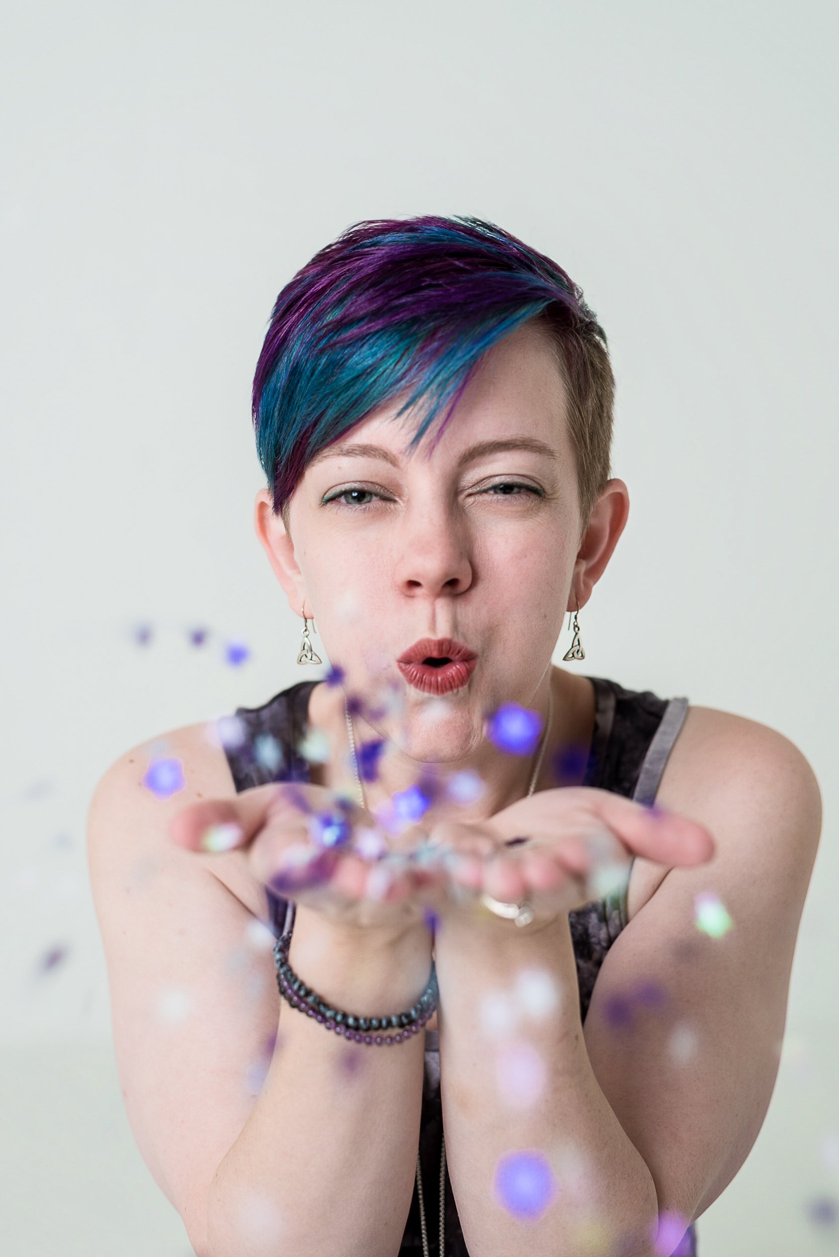 Playful studio portrait of Charlotte Harloff, Colorado Springs photographer, blowing glitter with a joyful, confident expression. A celebration of creativity, color, and soul-led self-expression.