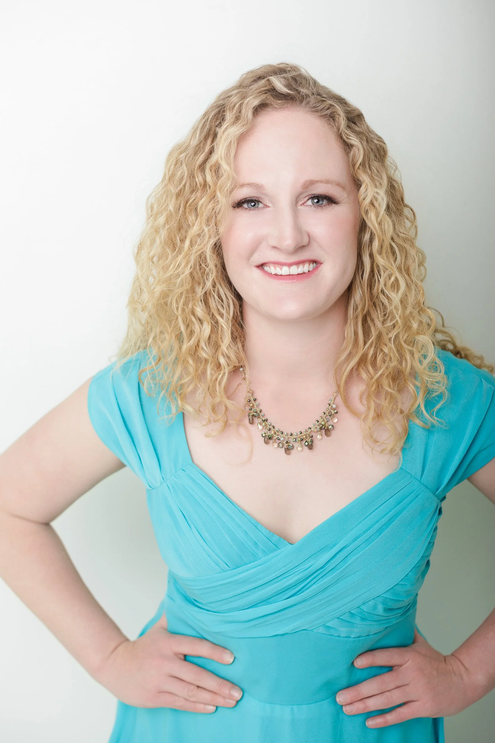 Smiling woman in turquoise dress and statement necklace posing confidently during a studio headshot session with Charlotte Harloff Portraits