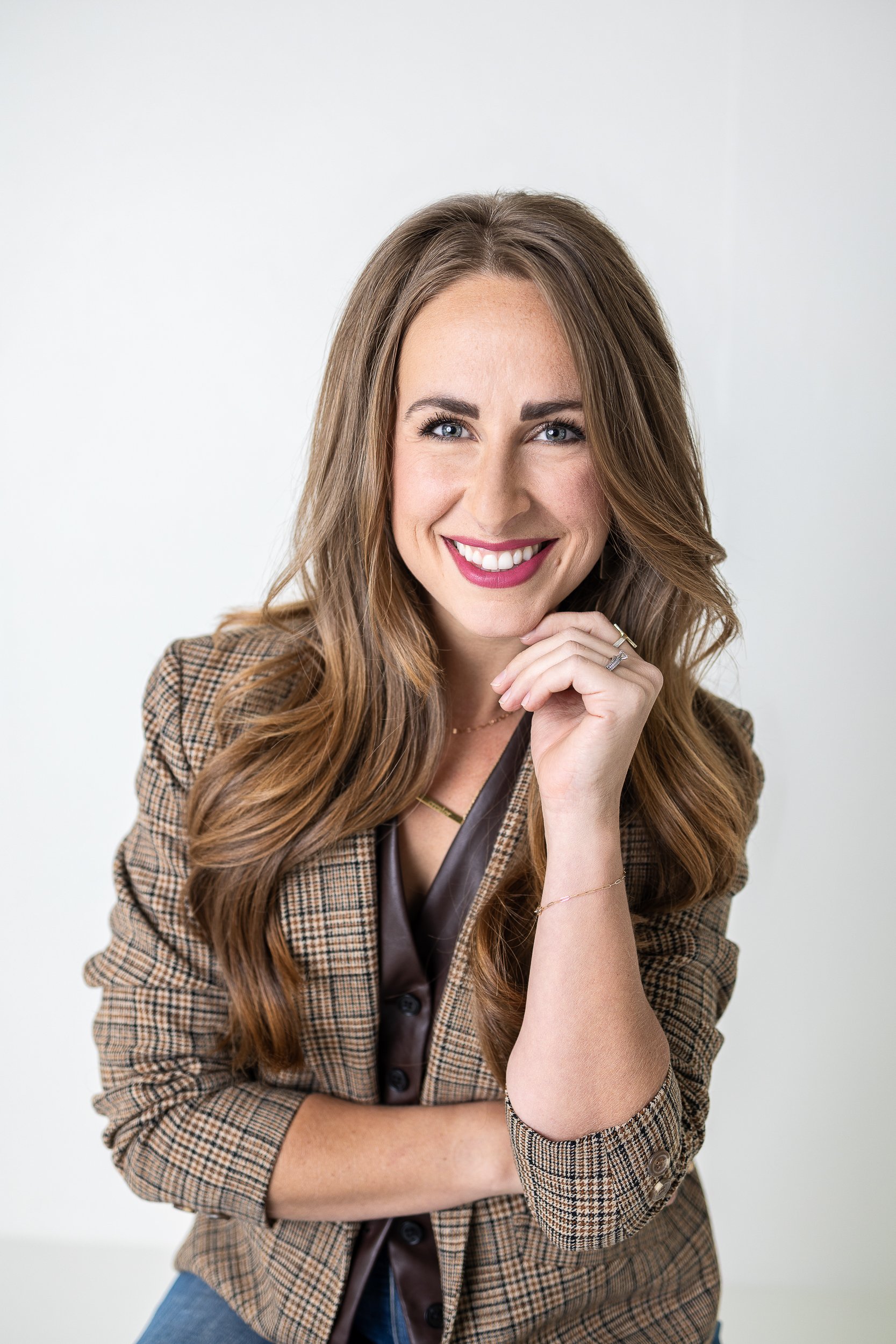 Confident woman in plaid blazer and satin top, smiling during a headshot session with Charlotte Harloff Portraits in Colorado Springs.