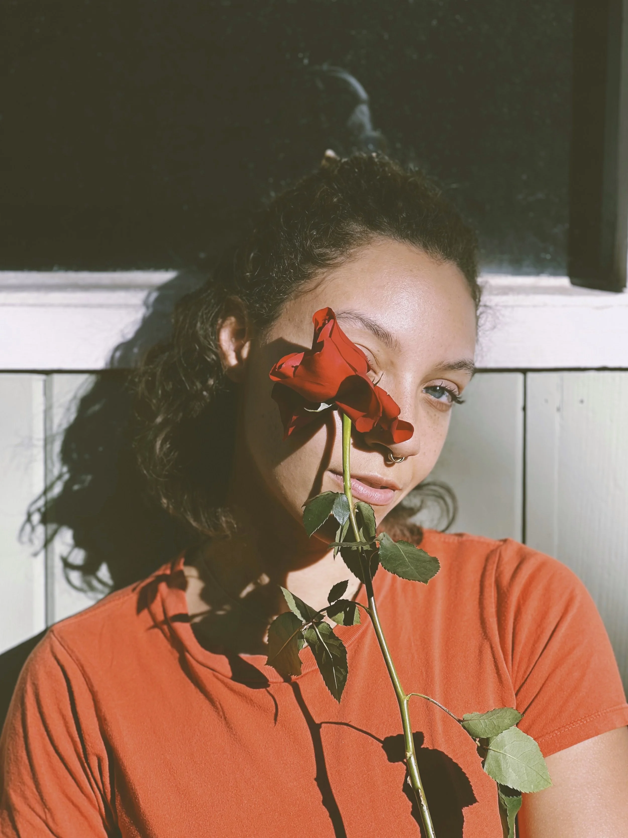 curly haired femme wearing a red shirt and holding a red rose
