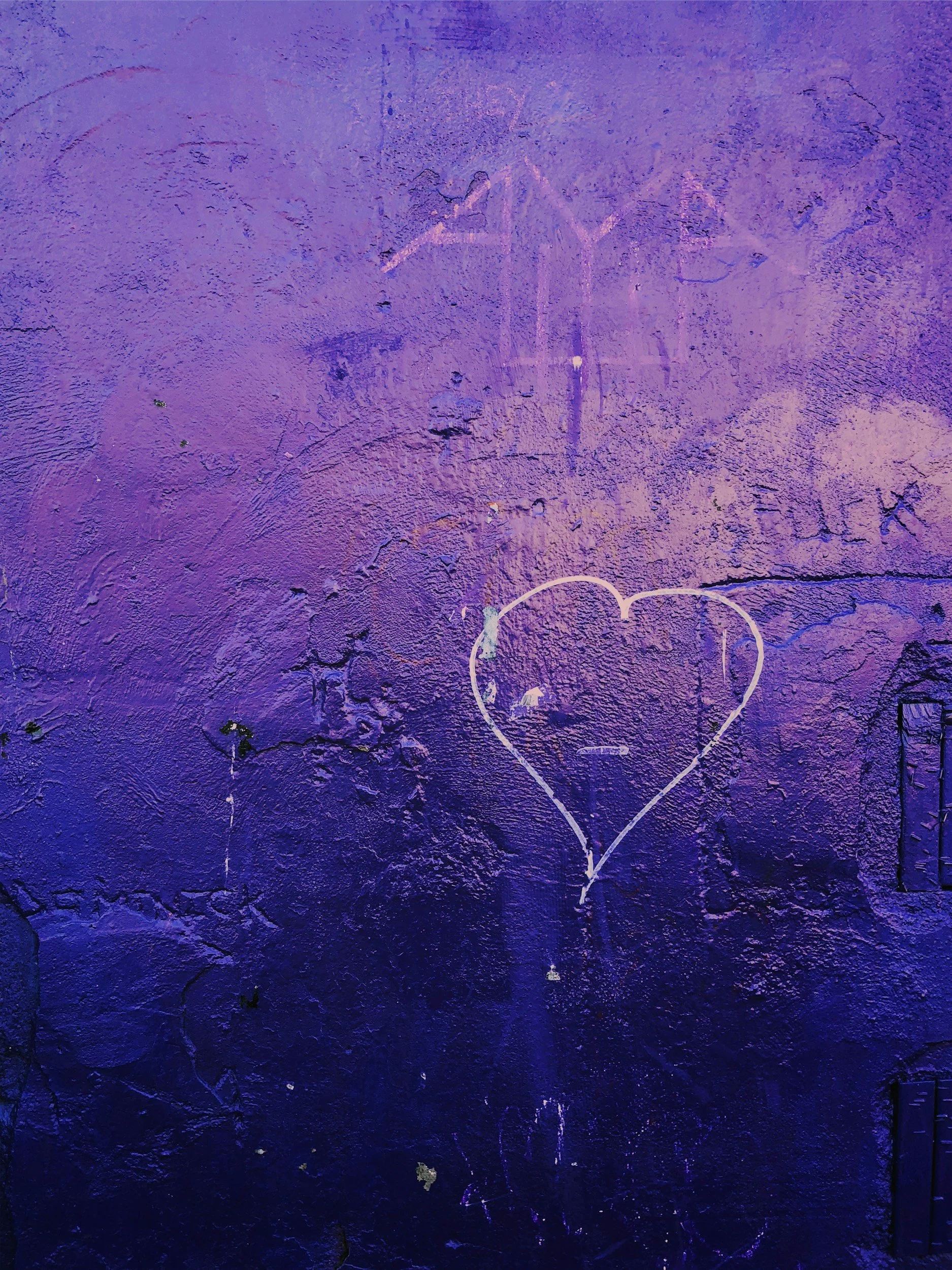 A textured purple wall with chalk or paint drawings, including a large heart and a faint angel figure above it.