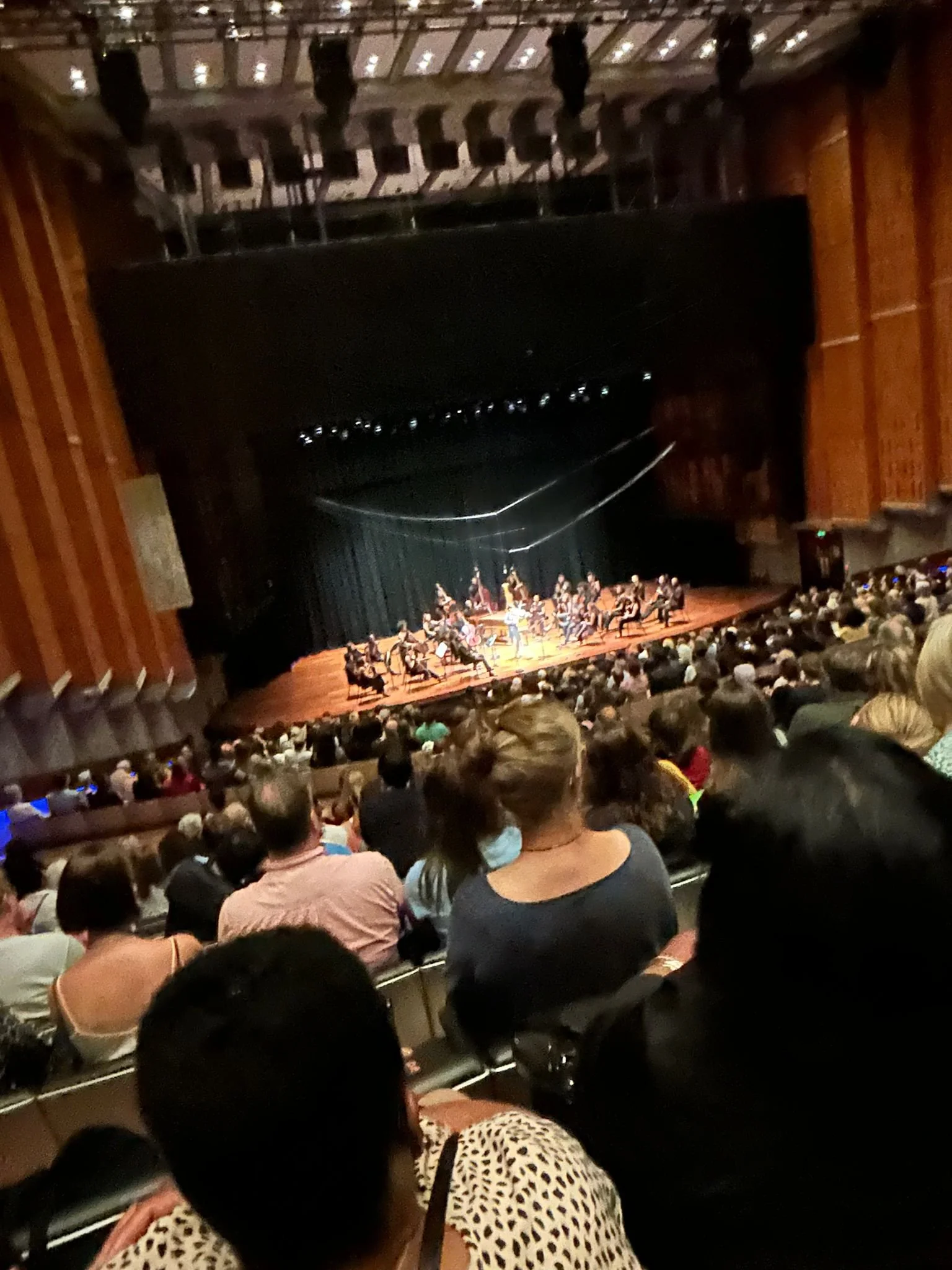 An audience watching an orchestra perform on stage in a concert hall.