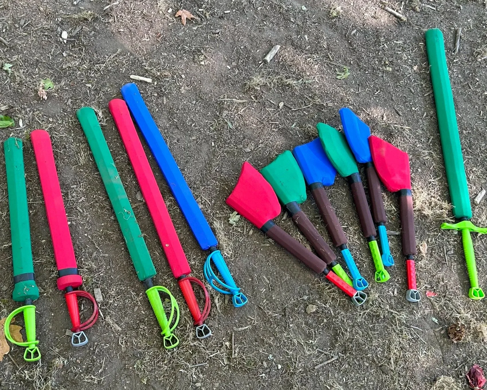 Colorful toy foam swords lying on dirt ground.