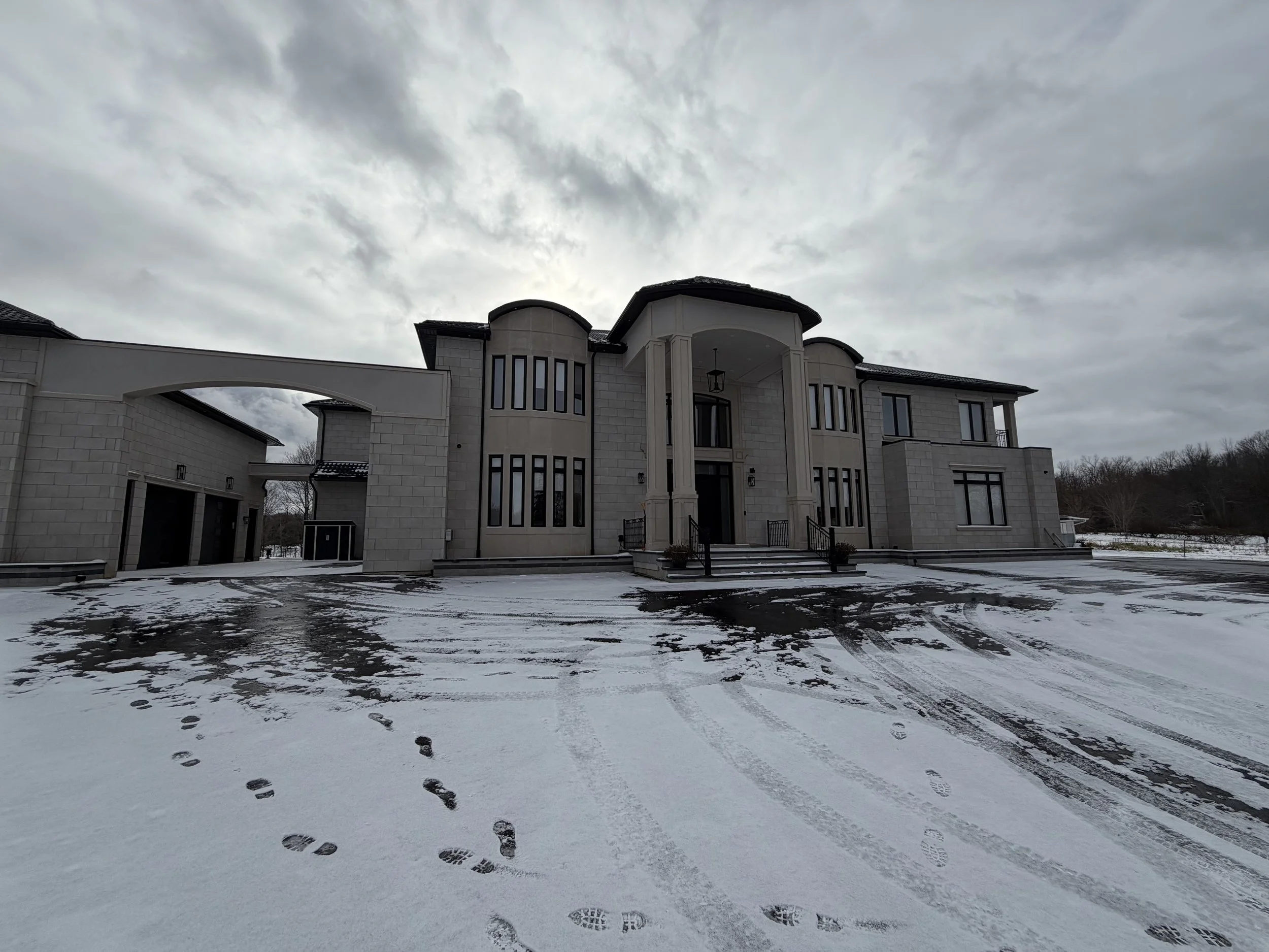 Large modern house with a snowy driveway and cloudy sky.
