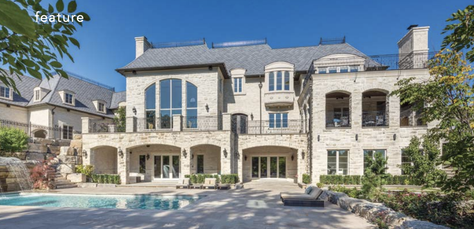 Large luxury house with stone exterior, multiple levels, and large windows, surrounded by trees and a pool in the backyard.