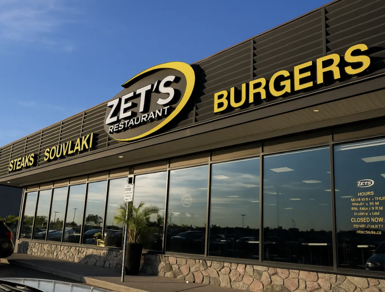Exterior view of Zets Restaurant with signage for steaks, souvlaki, and burgers, large glass windows, and a small potted plant outside.