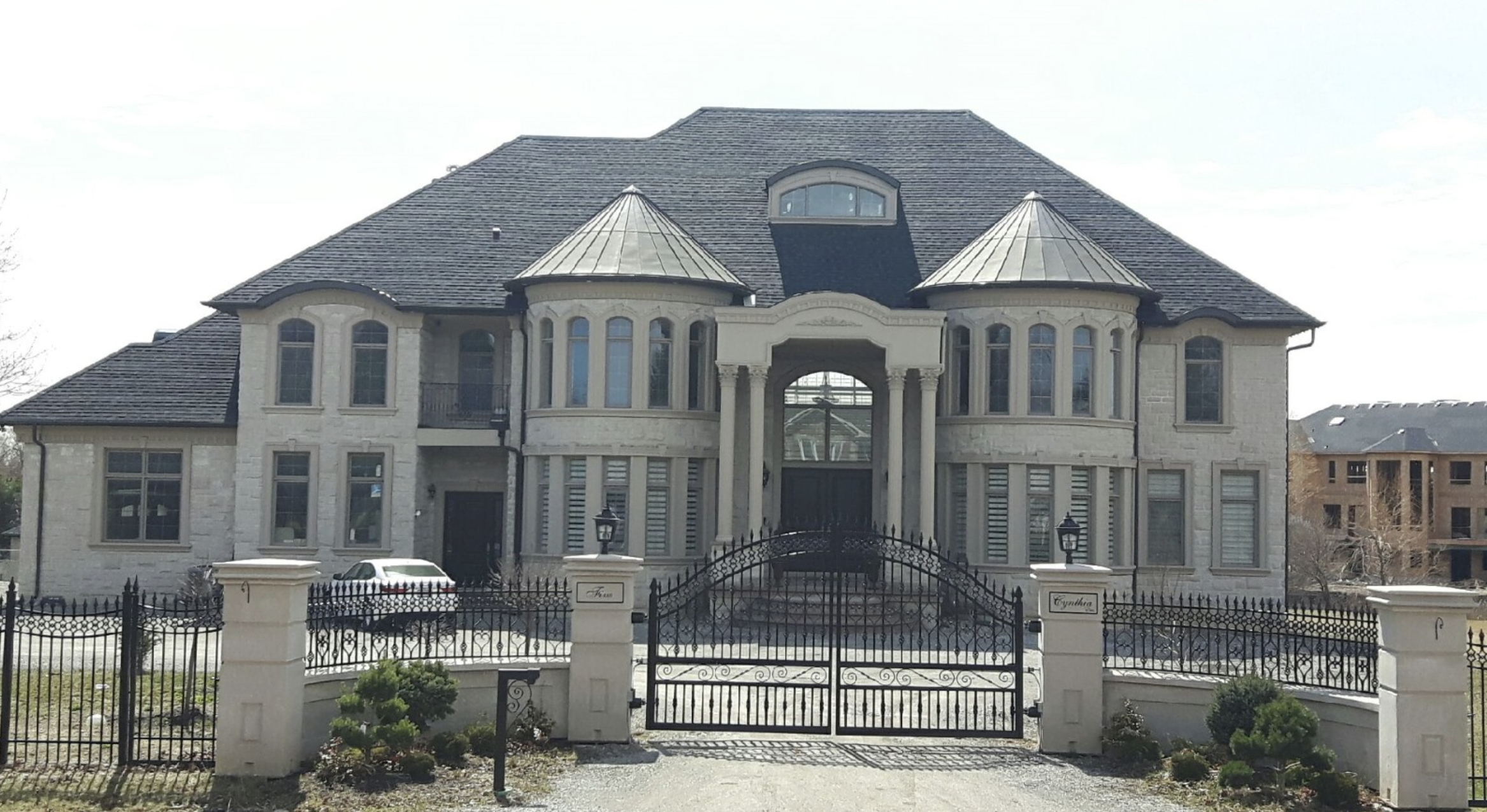 A large, ornate mansion with a gated front yard, stone exterior walls, multiple windows, and a prominent entrance supported by columns.