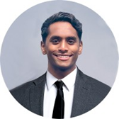 Professional headshot of a man in a suit and tie smiling against a gray background.