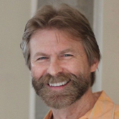 A smiling man with a beard and light brown hair, wearing a light orange shirt.