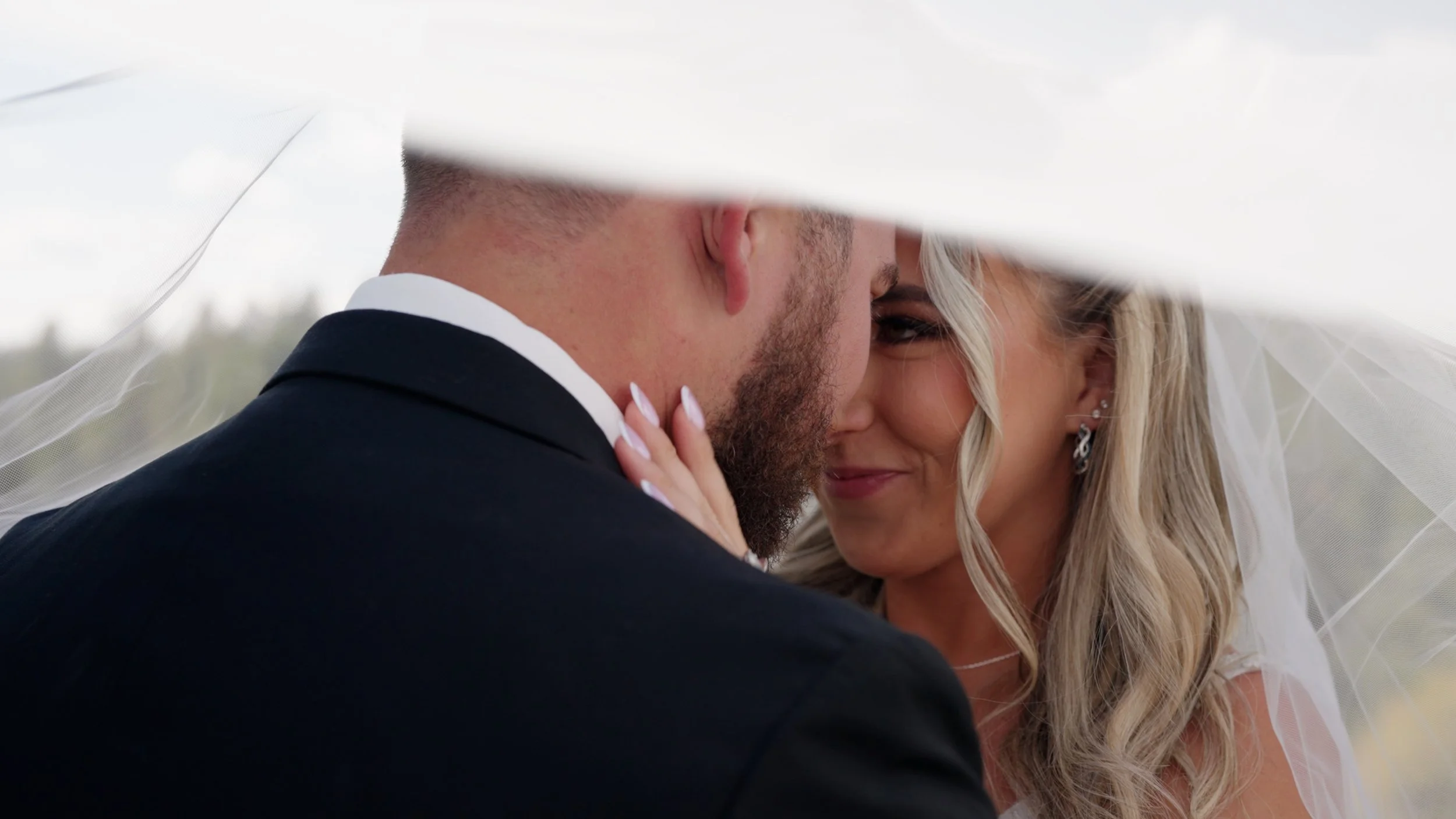 A bride and groom close together under a veil, smiling at each other during a wedding.
