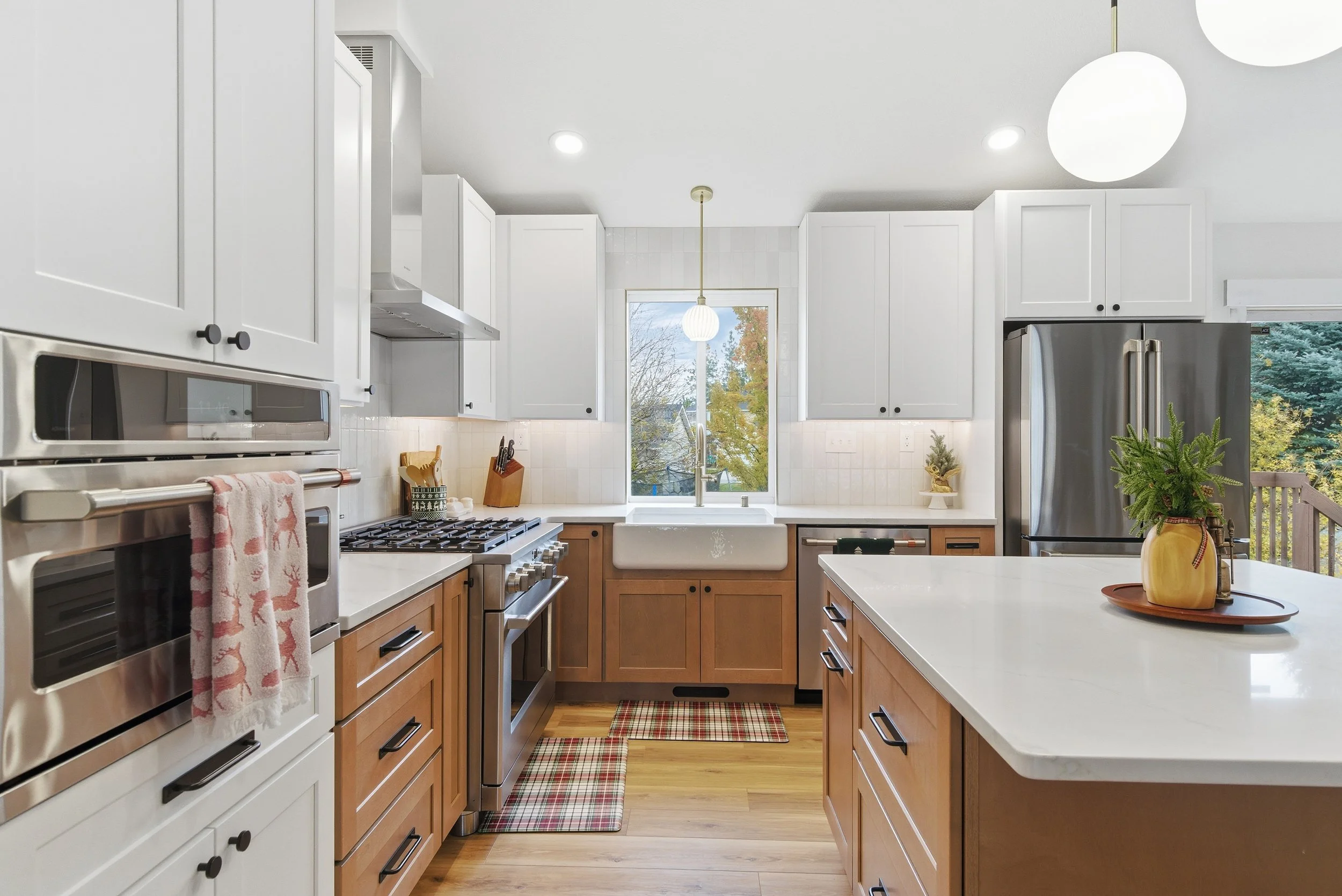 Modern kitchen with white and wooden cabinets, stainless steel appliances, a large island, and a window overlooking trees.
