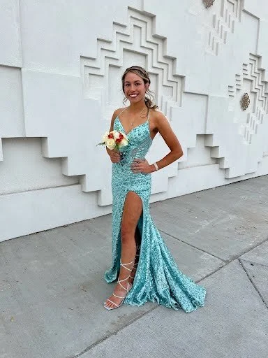 Young woman in a glittery blue evening gown standing outside, holding a bouquet of flowers, smiling
