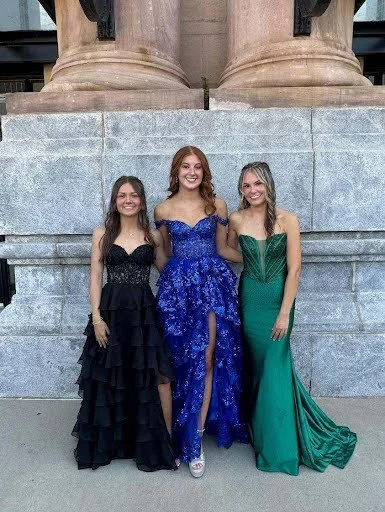 Three women in formal evening gowns standing in front of stone steps and columns.