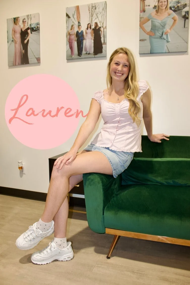 A woman with blonde hair wearing a black sleeveless top and black pants, standing and smiling in a modern room with framed photos on the wall. The photo includes decorative graphic elements, such as a pink leaf, a pink cloud shape, and the name "Brenna" in pink text at the bottom.