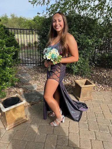 Young woman in a fancy dress holding a bouquet of flowers outdoors near a gate and greenery.