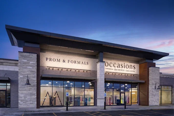 Exterior view of a clothing store called 'Occasions by Dress Gallery' selling prom and formal dresses, with large glass windows and signs indicating the sale of prom, formals, and occasions