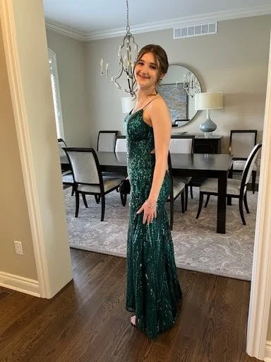 Young woman in a green evening gown standing in a dining room, smiling at the camera
