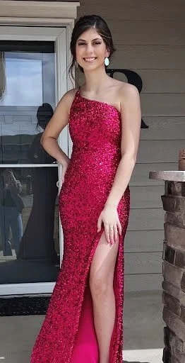 A young woman in a shiny pink strapless gown with a thigh-high slit, standing on a porch.