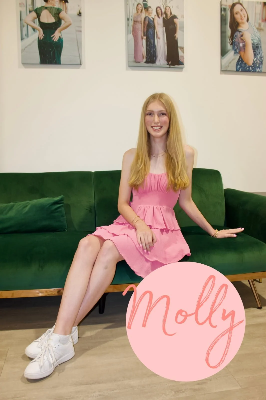 A young woman with long, dark hair sits on a green velvet chair in a room with a white wall. She is smiling and wearing a white long sleeve shirt, a brown vest, black pants, and sneakers. There is a framed photo of two women in dresses on the wall, a black nightstand with gold handles, a green curtain, and decorative pink clouds and butterfly graphics on the image. The name 'Caroline' is written at the bottom in pink letters.