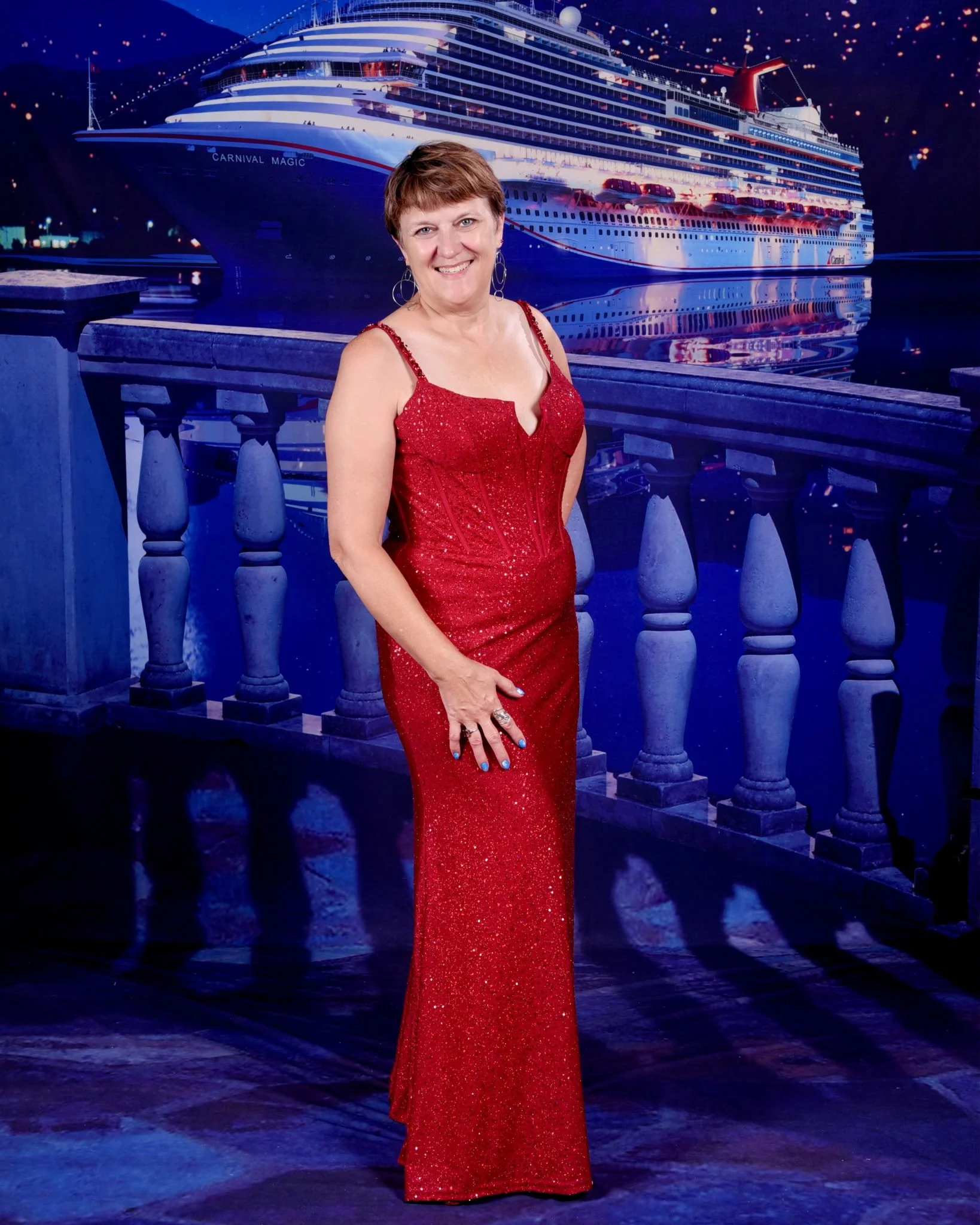 A woman in a red sequined gown standing on a wooden deck with a large cruise ship named Carnival Magic in the background.