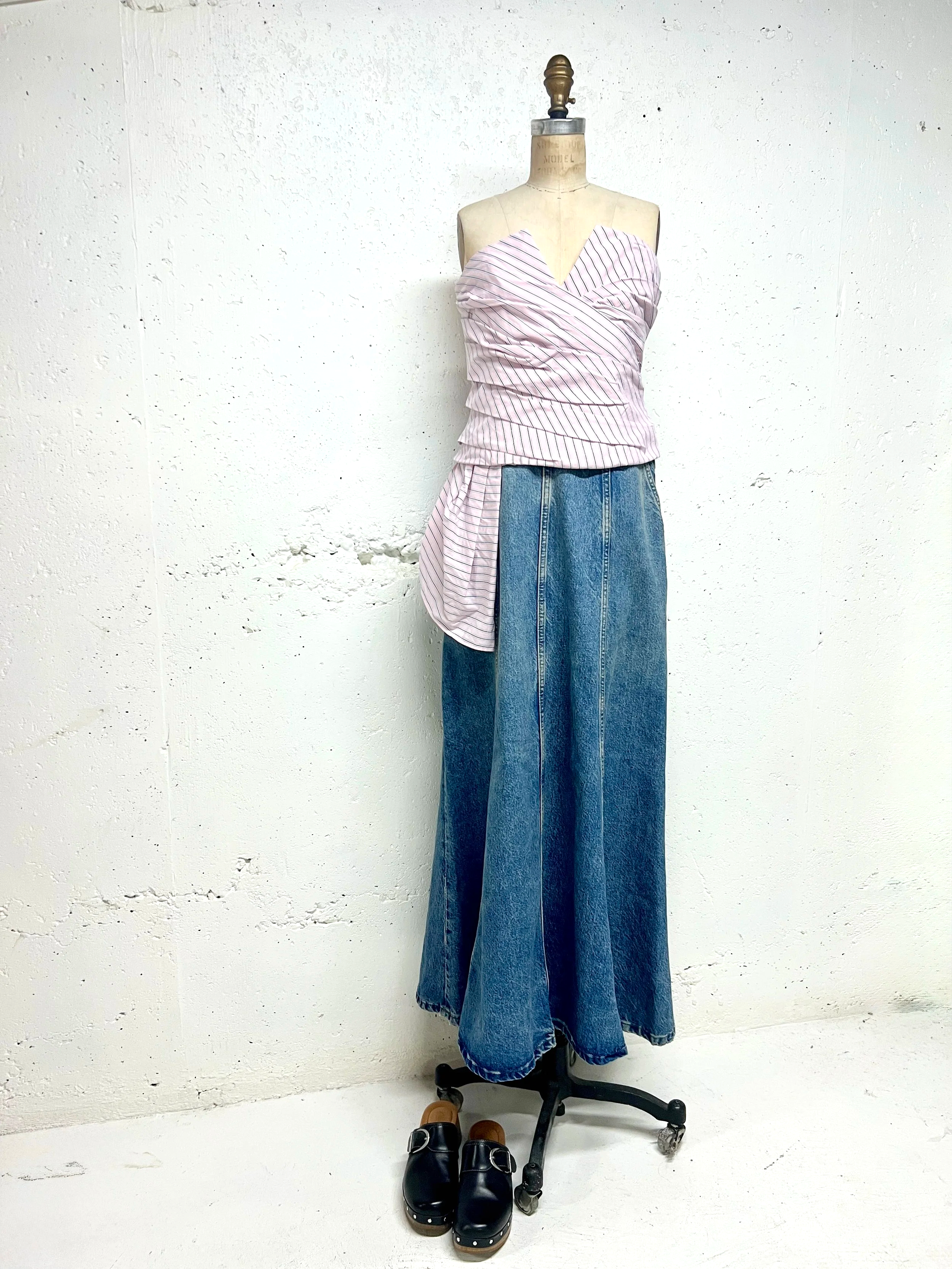 Mannequin dressed in a pink and white striped off-shoulder top with a long tail on one side, and high-waisted wide-leg blue jeans, standing against a white wall with black loafers on the floor.