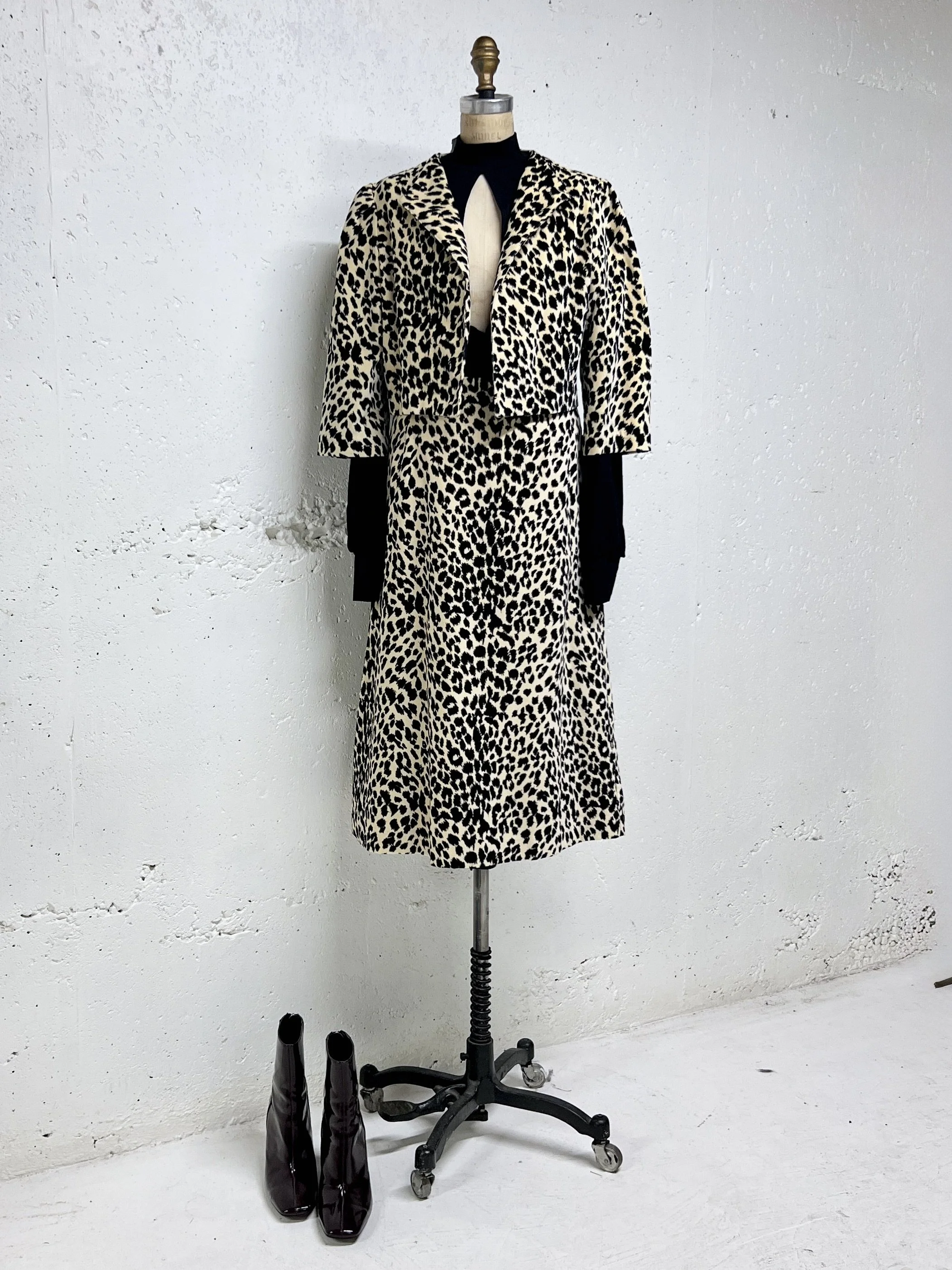 Leopard print coat and skirt set on mannequin, black top underneath, with brown ankle boots on white floor against a white wall.