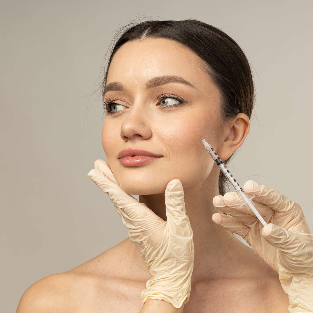 A woman receives a cosmetic injection in her cheek from a medical professional wearing latex gloves.