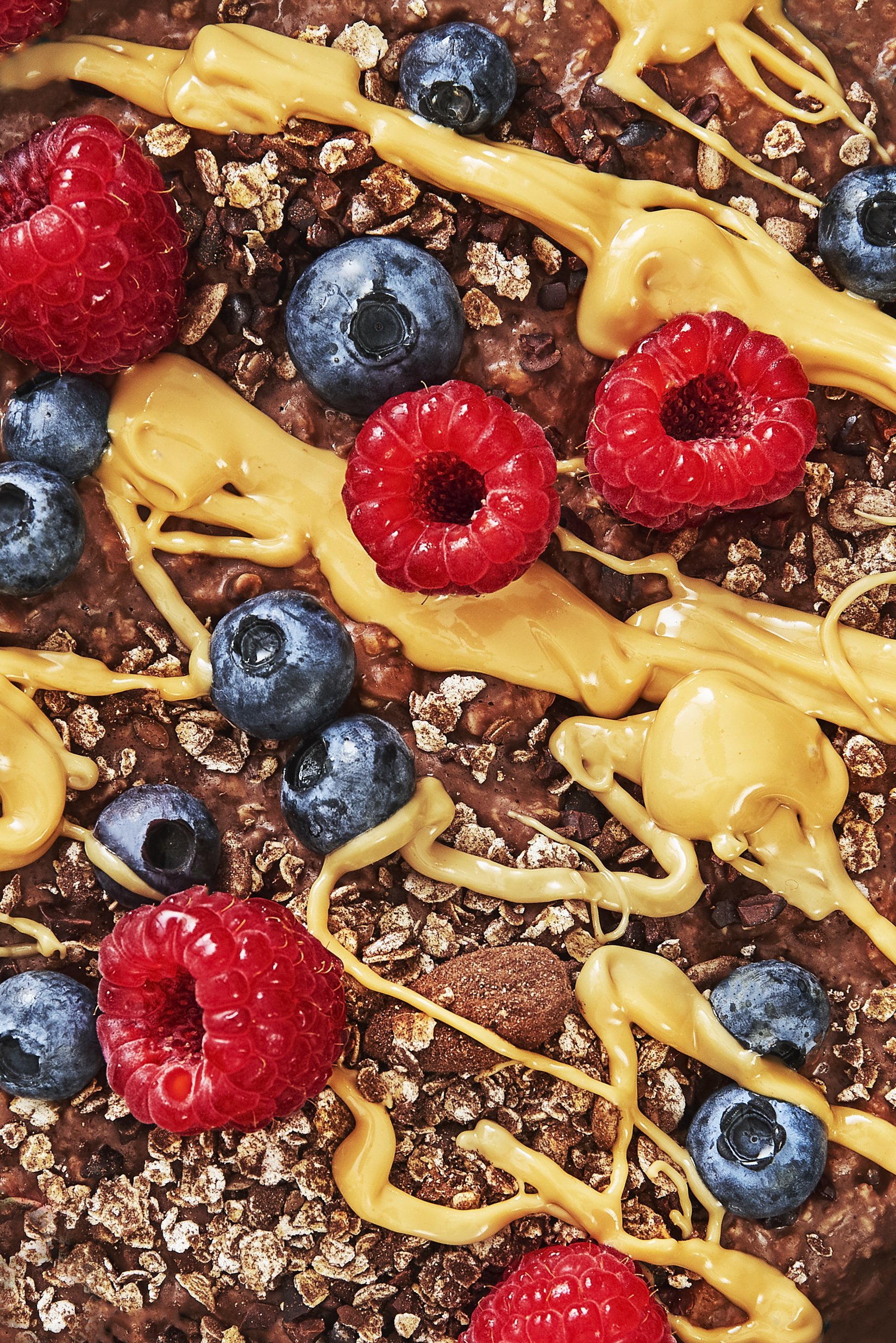 Nahaufnahme eines Schokoladenkuchens mit Himbeeren, Blaubeeren, Schokoladenstückchen und einer Marzipan- oder Kuchenglasur in gelber Farbe.