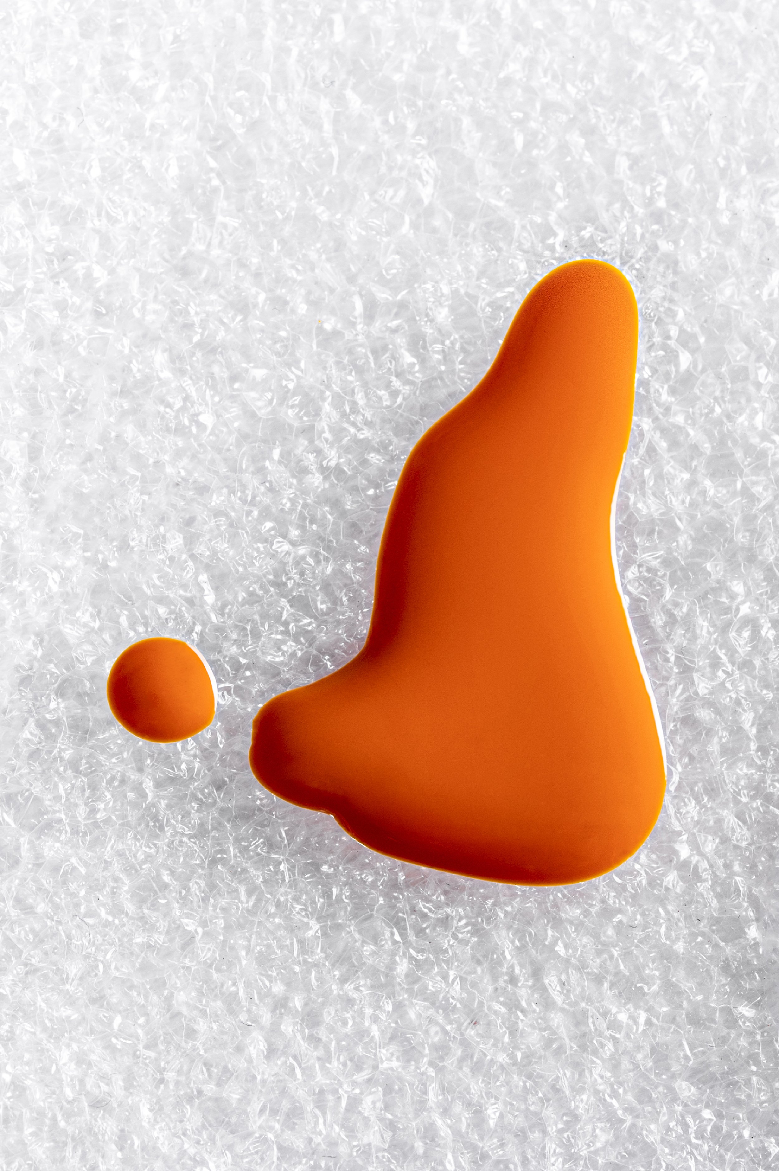 Ein orangefarbener Wassertropfen auf einer Schneefläche.