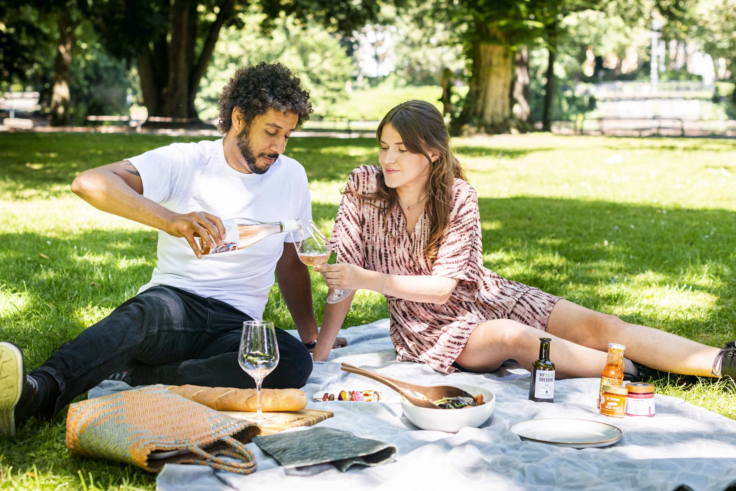 Ein Mann und eine Frau entspannen sich bei einem Picknick im Park. Der Mann gießt Wein in das Glas der Frau, während sie auf einer Decke sitzen.