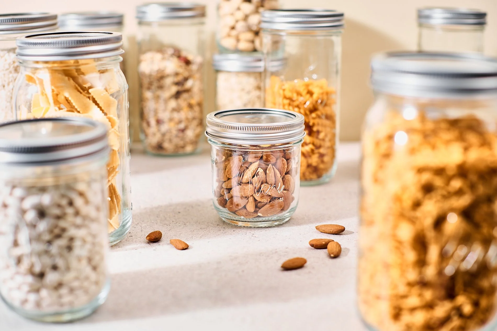 Mehrere Gläser mit verschiedenen getrockneten Lebensmitteln auf einer hellen Oberfläche, einige zerstreut davor.