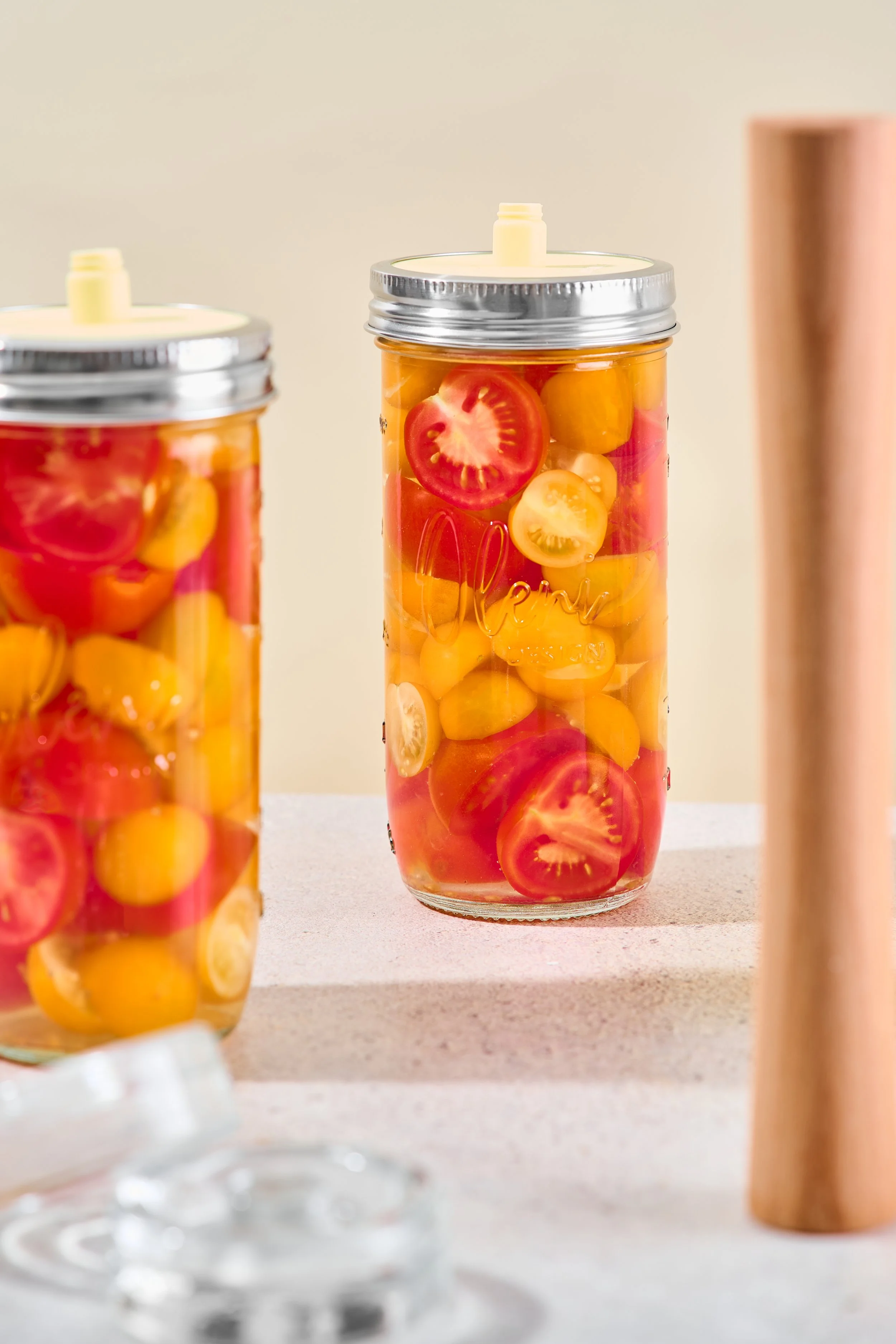 Ein Glas mit eingelegten Tomaten und gelben Cherrytomaten, verschlossenen mit einem Deckel, auf einer hellen Oberfläche.