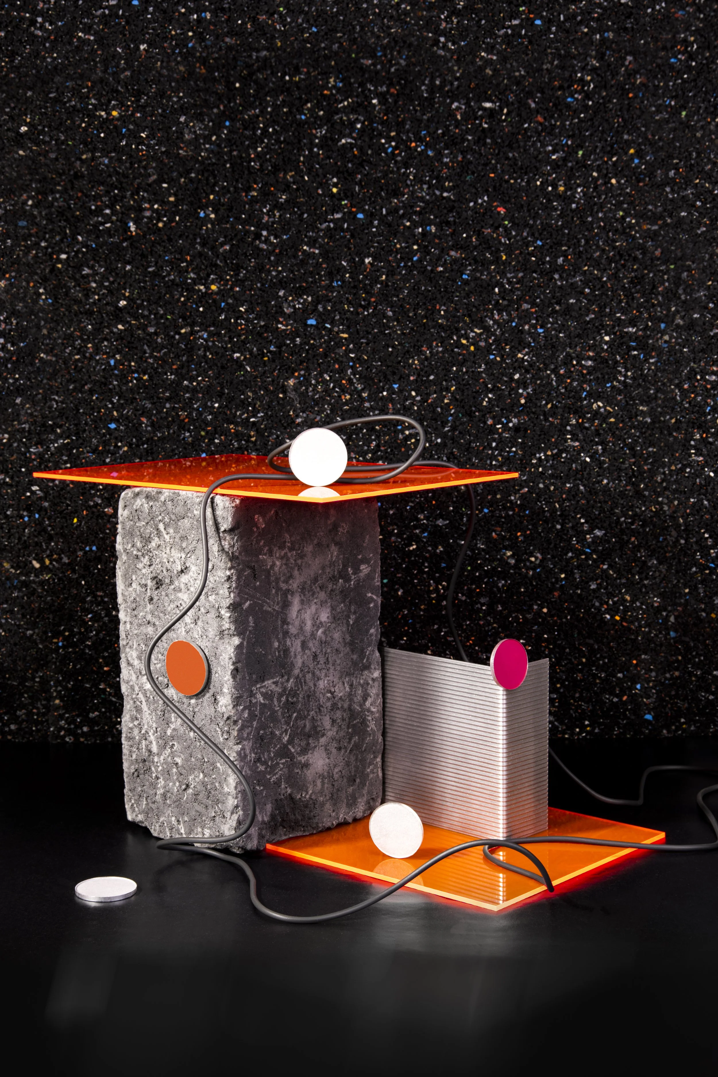 Kunstinstallation mit geometrischen Objekten, Lichter und Kabel vor schwarzem Hintergrund.