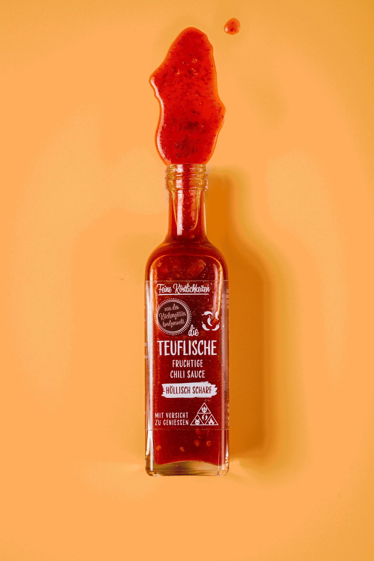 Flasche mit roter Chili-Sauce, die an den Rand aufgeschoben ist, auf orangefarbenem Hintergrund.