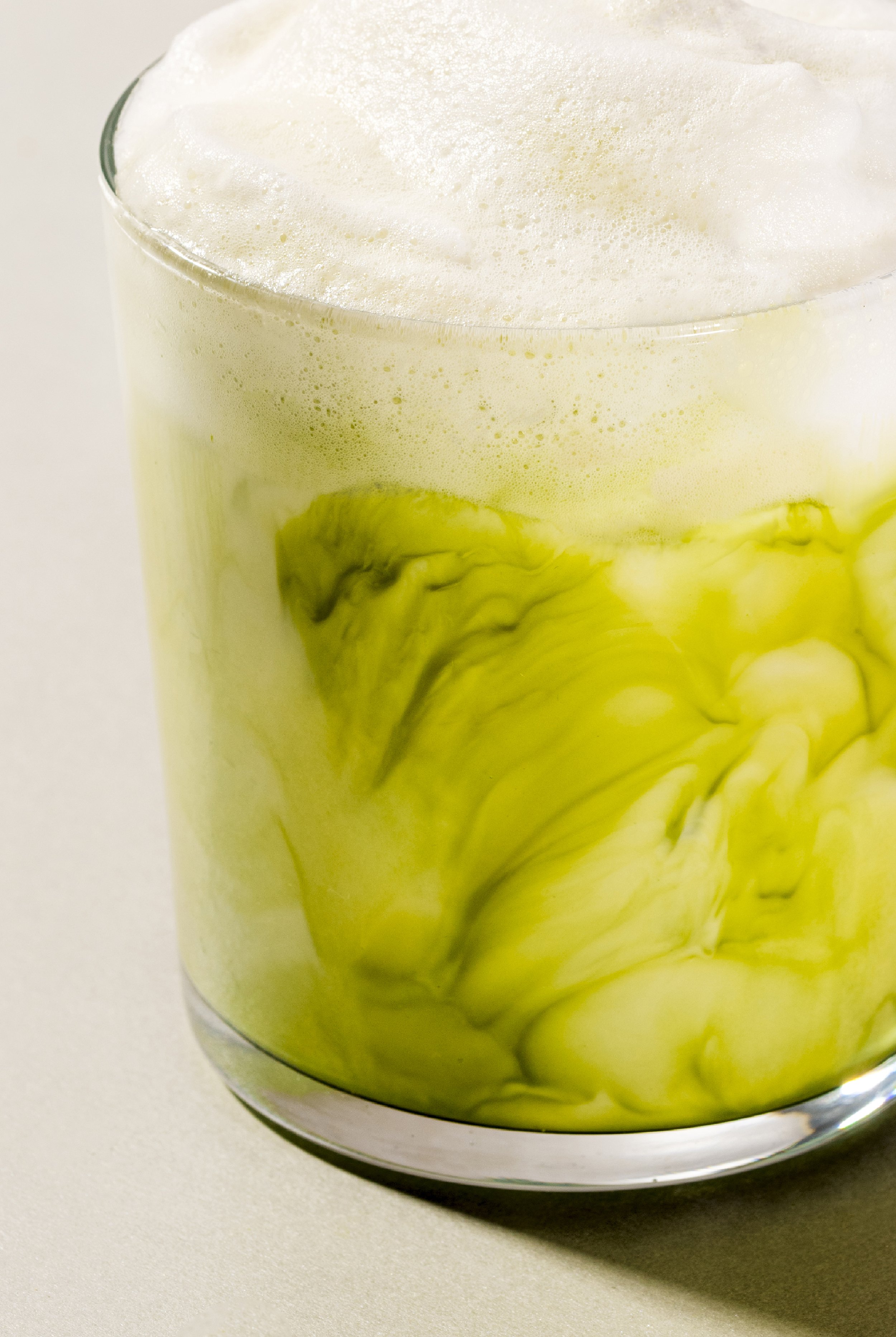 Ein Glas mit einem grünen, gelb verquirltem Getränk, das oben schäumt.