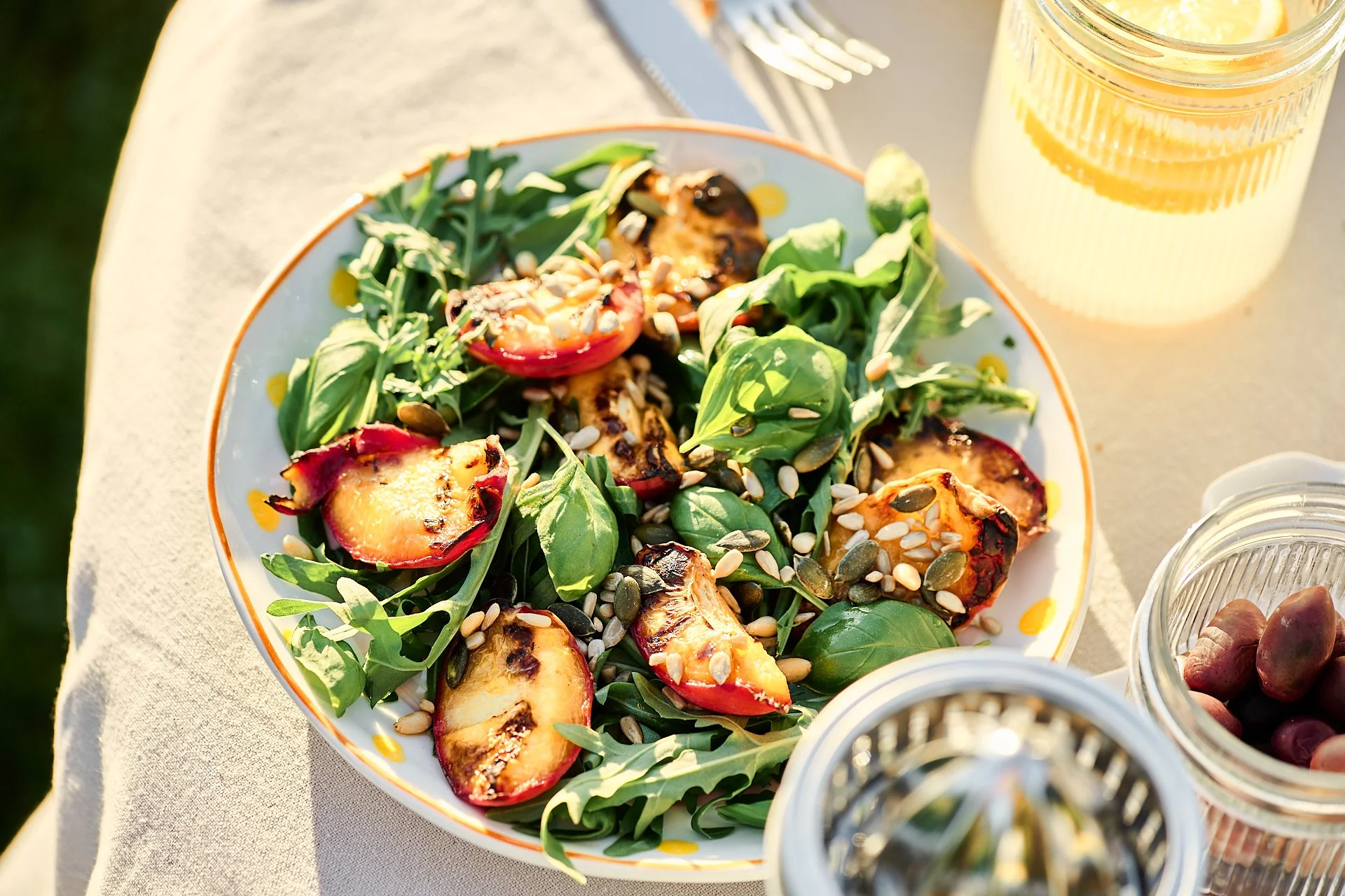 Bunter Salat mit Tomaten, Rucola, Sonnenblumenkerne und anderen frischen Zutaten auf einem Teller, neben einem Glas Zitronenlimonade.