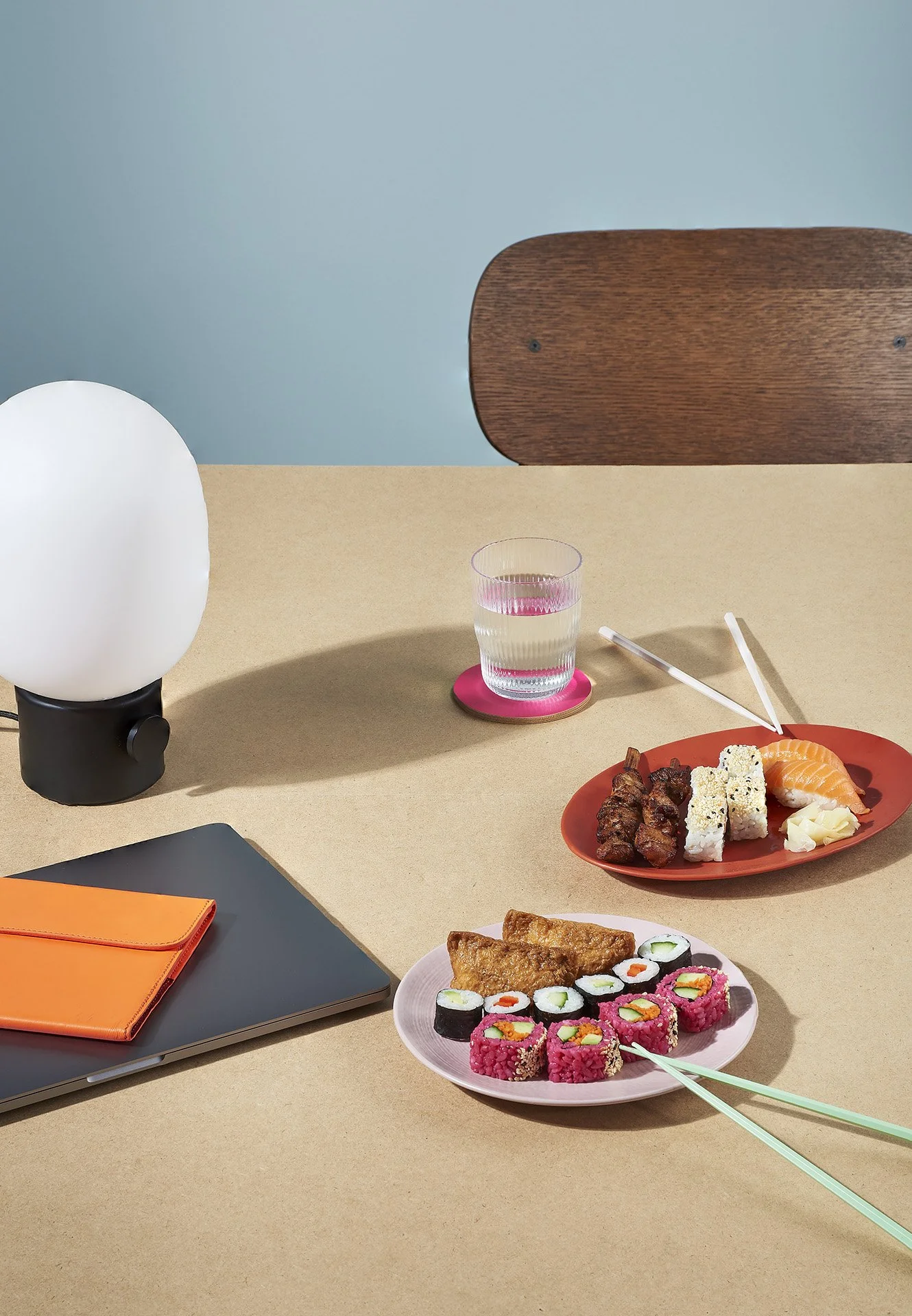 Tisch mit Sushi, Wasser, Laptop, ovale Lampe, Pappette, und Schreibwaren