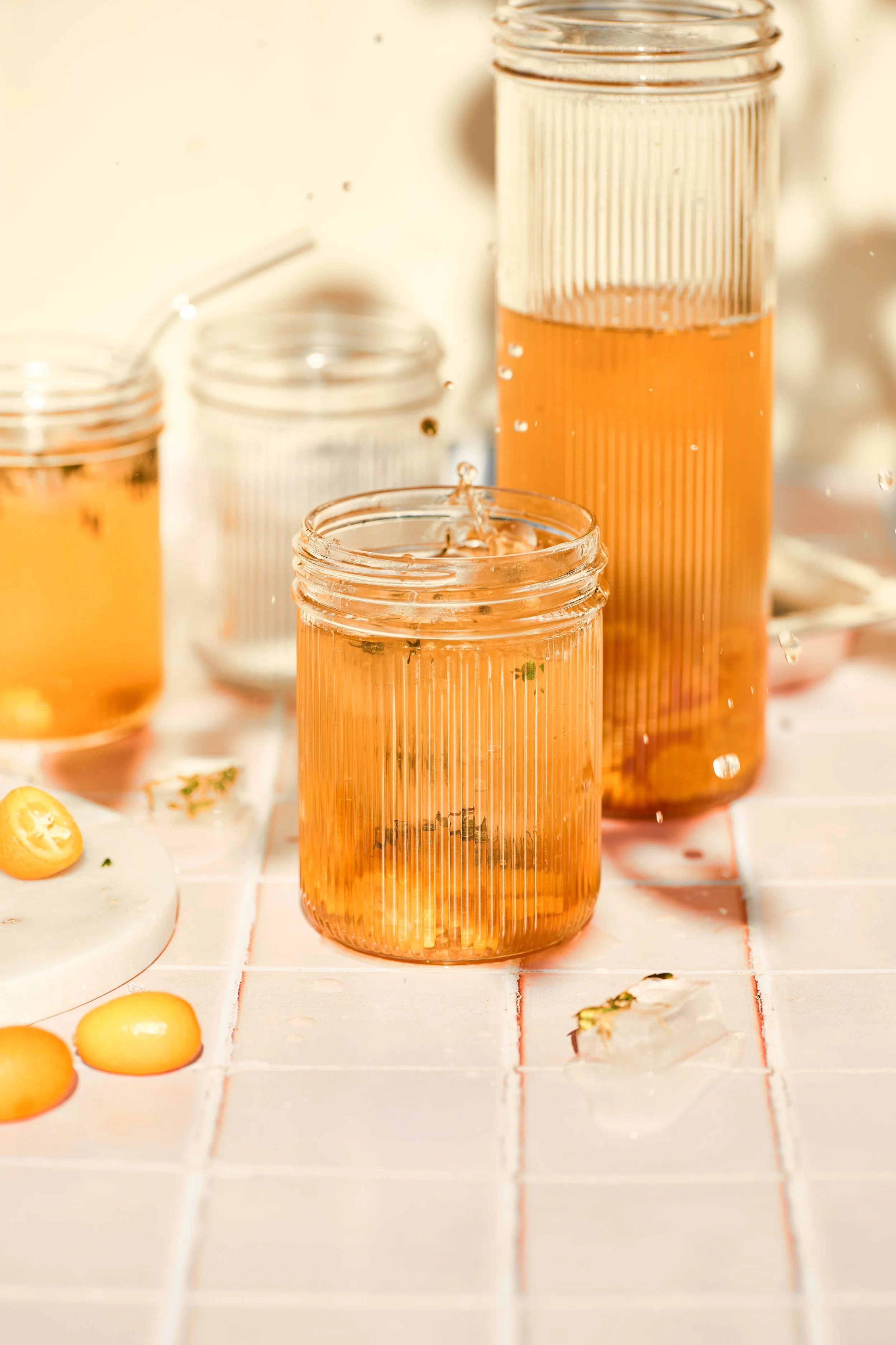 Mehrere Gläser mit pinkfarbenem Getränk auf einer weißen Fliesenoberfläche, einige Zitronenscheiben und -schnitze sind sichtbar.