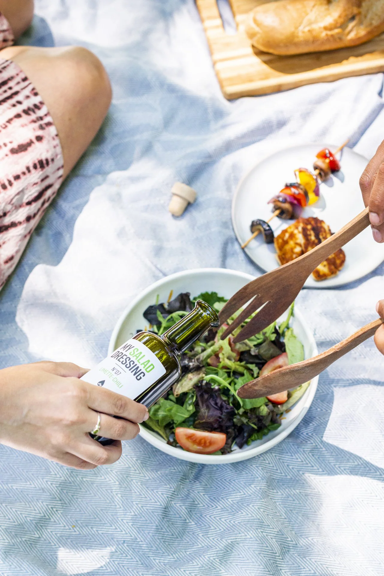 Person, die eine grüne Salatsauce auf einen grünen Salat gießt, während andere Personen an einem Picknicktisch sitzen.