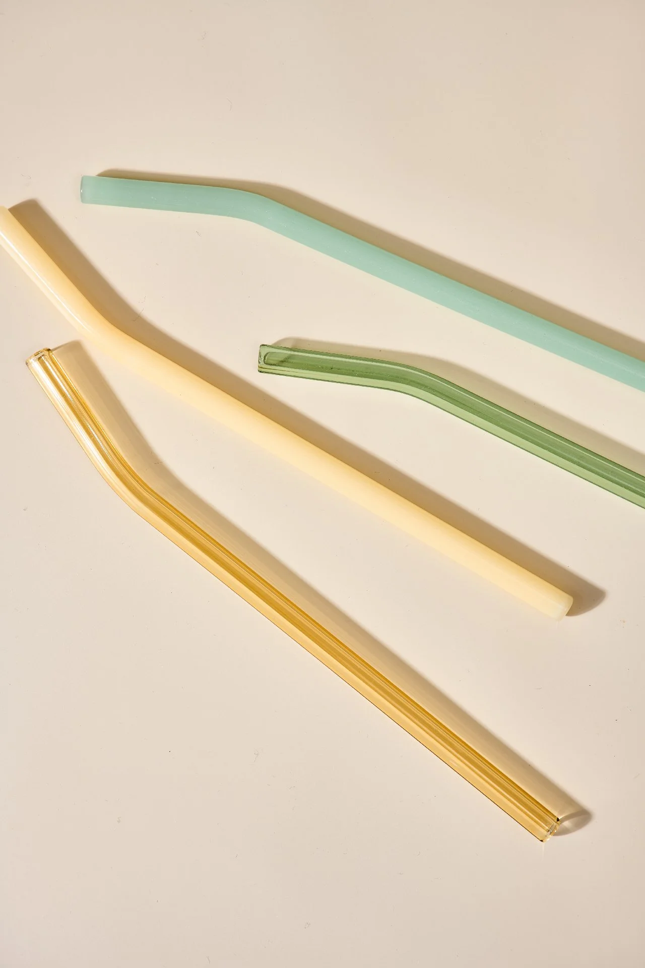 Drei bunte, gebogene Glasstrohhalme in Pastellfarben auf weißem Hintergrund.